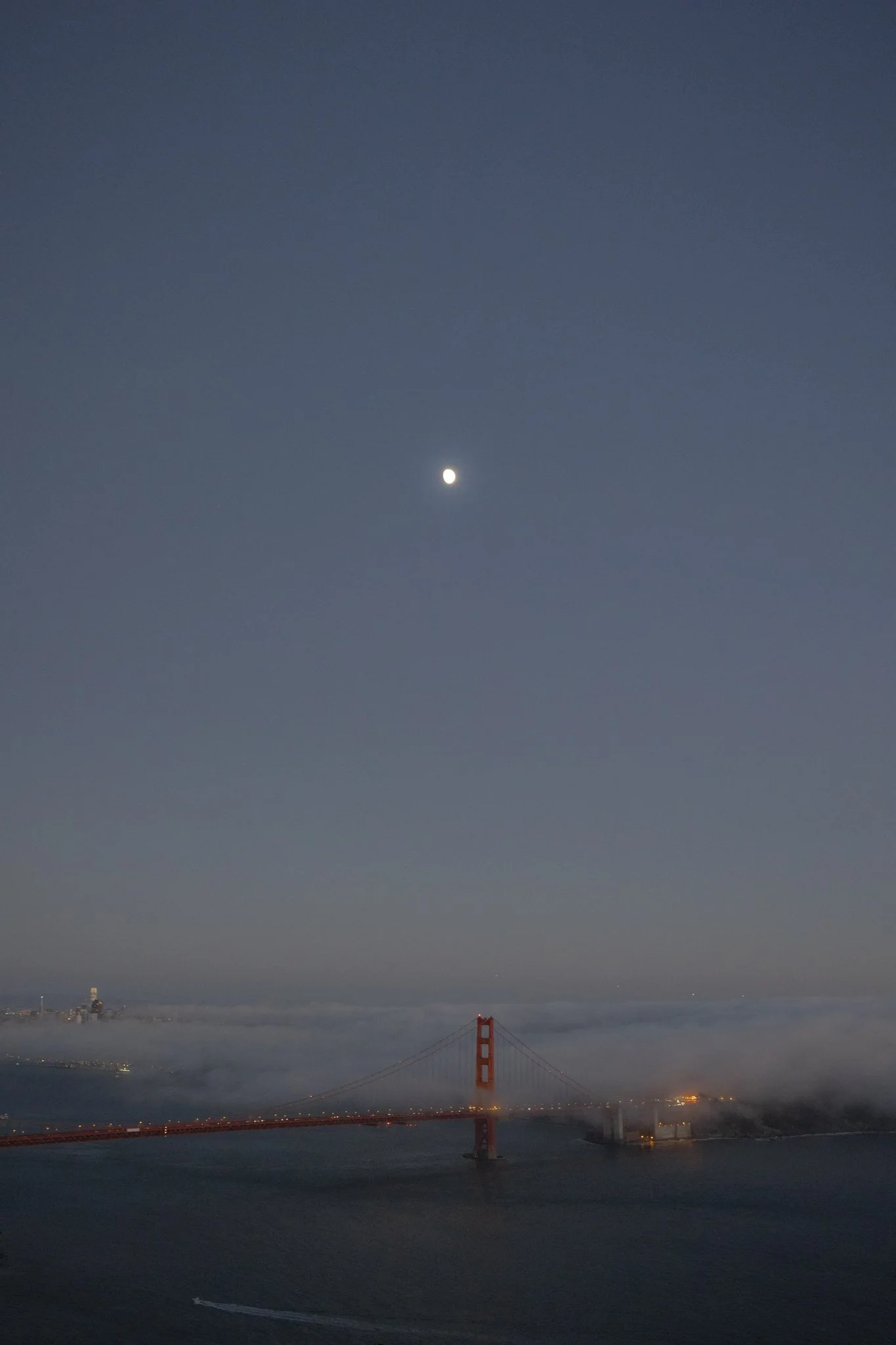 A view of the Golden Gate Bridge in San Francisco at night with the moon in the sky above the bridge.