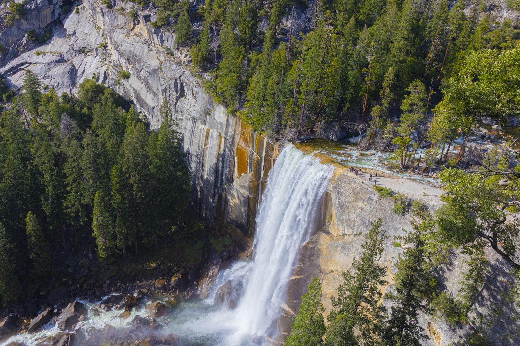 An aerial view of a waterfall cascading down a rocky cliff surrounded by dense green forest.