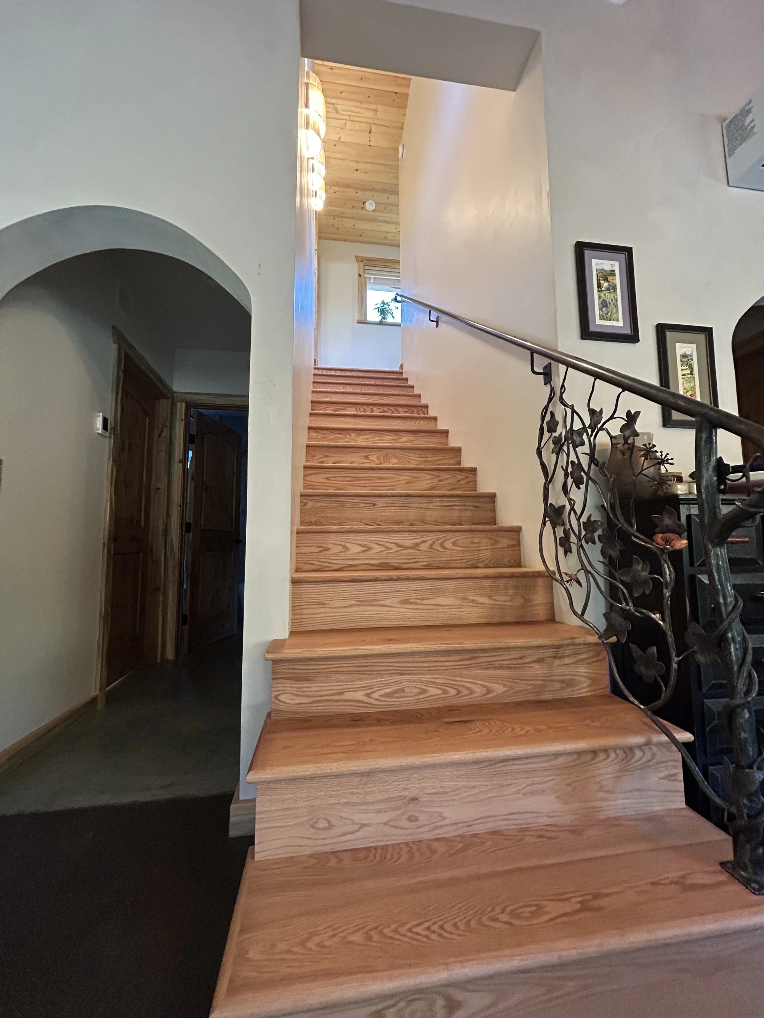 Wooden staircase with black wrought iron railings and framed pictures on a white wall.
