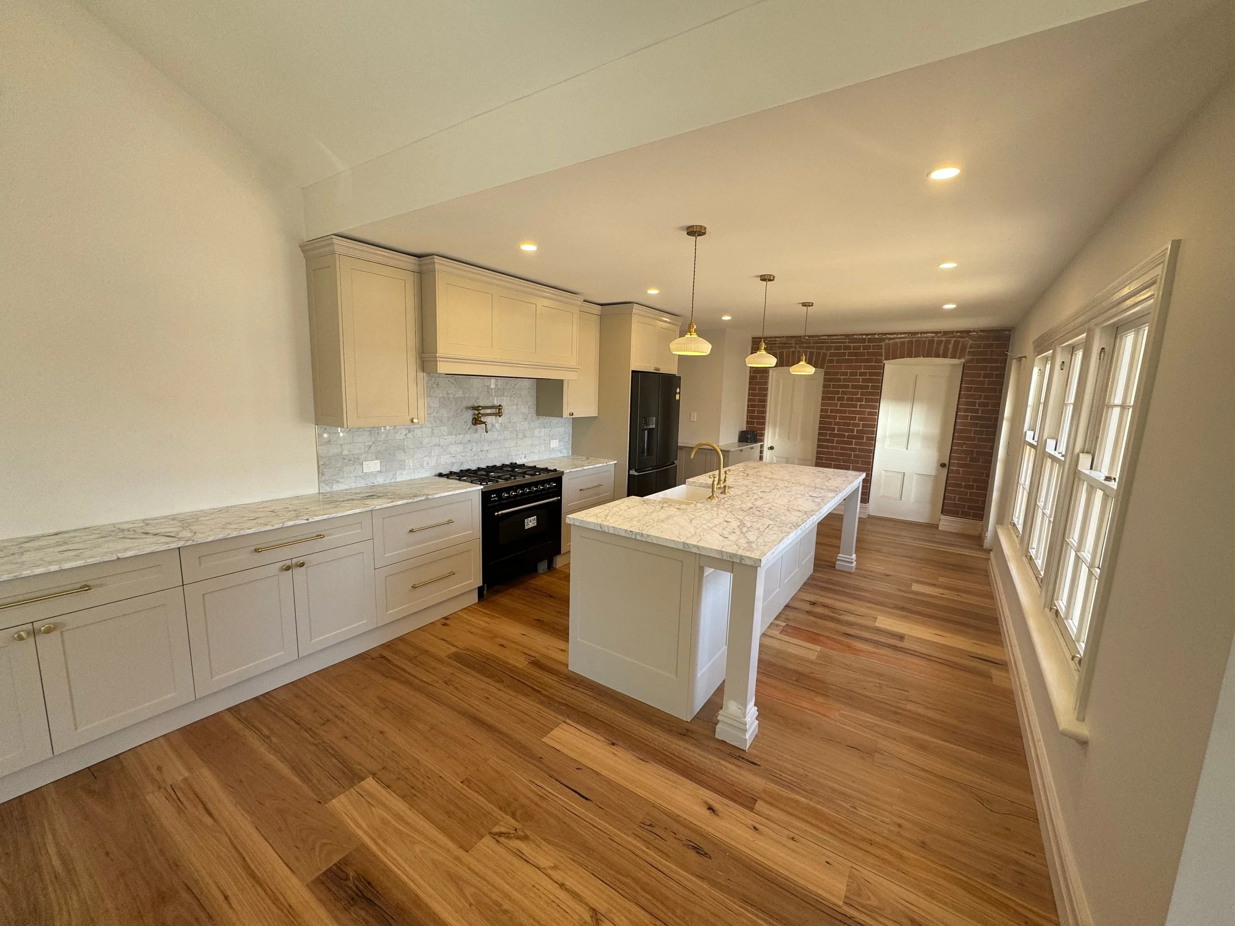 A modern kitchen with white cabinets, marble countertops, a black stove, a black refrigerator, pendant lights, and windows with multiple panes.