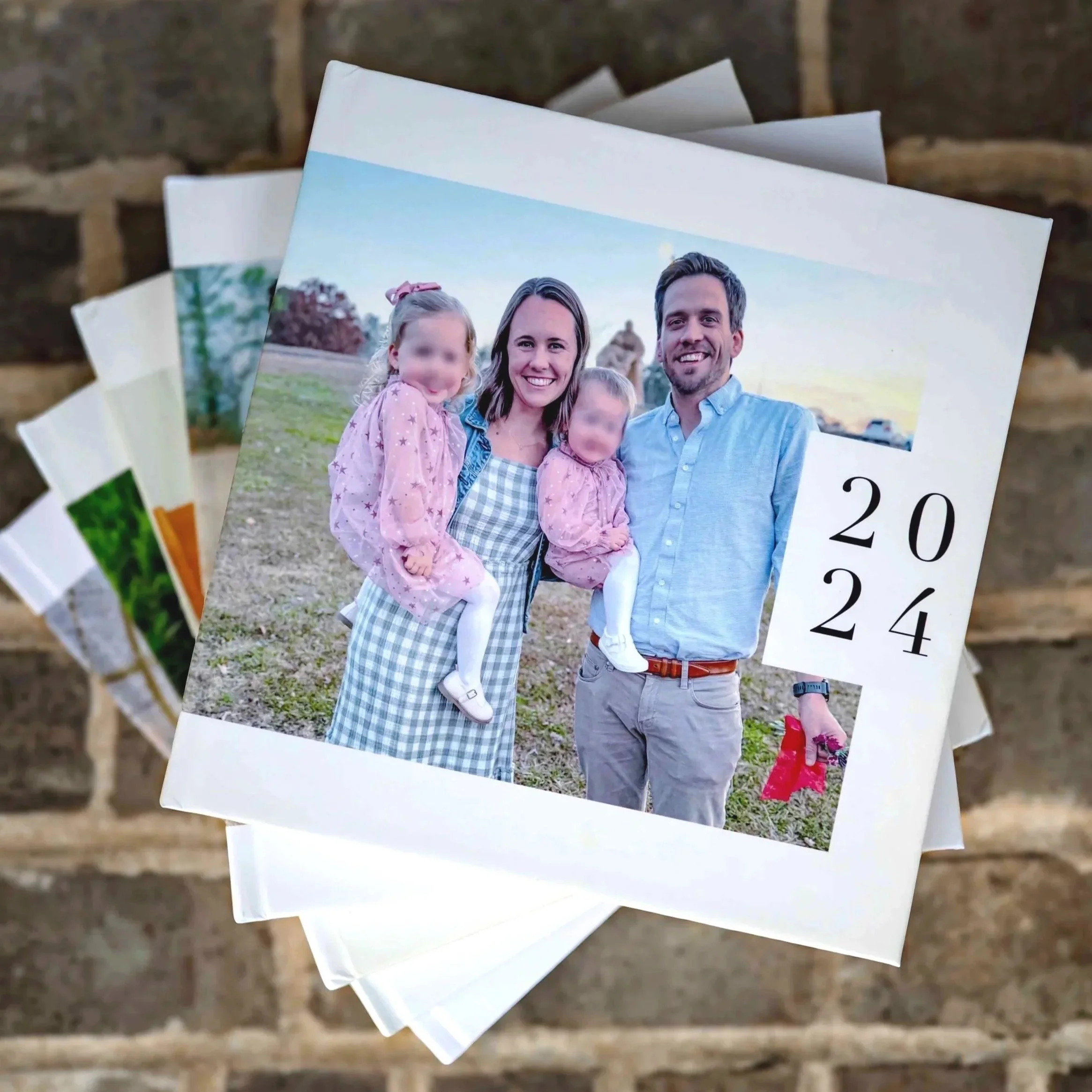 Close-up of a pile of printed photos on a wooden surface, featuring a happy family outdoors, with a woman, man, and young children smiling.