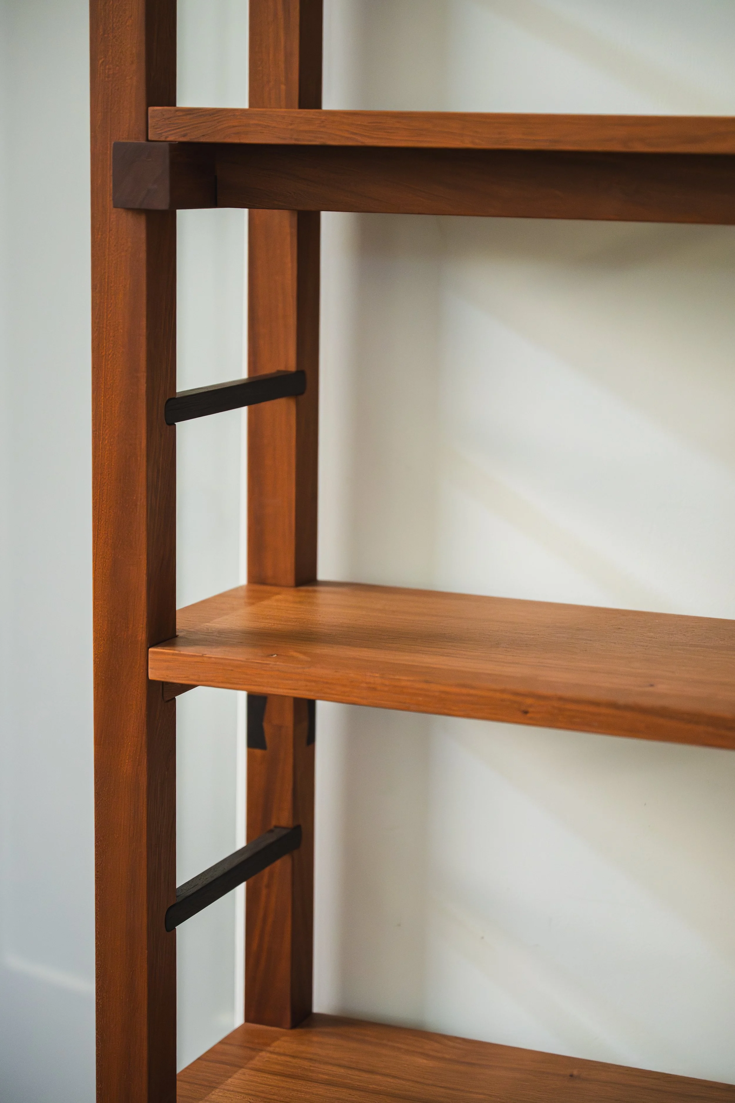 Close-up of a wooden shelving unit with three shelves, against a plain off-white wall.