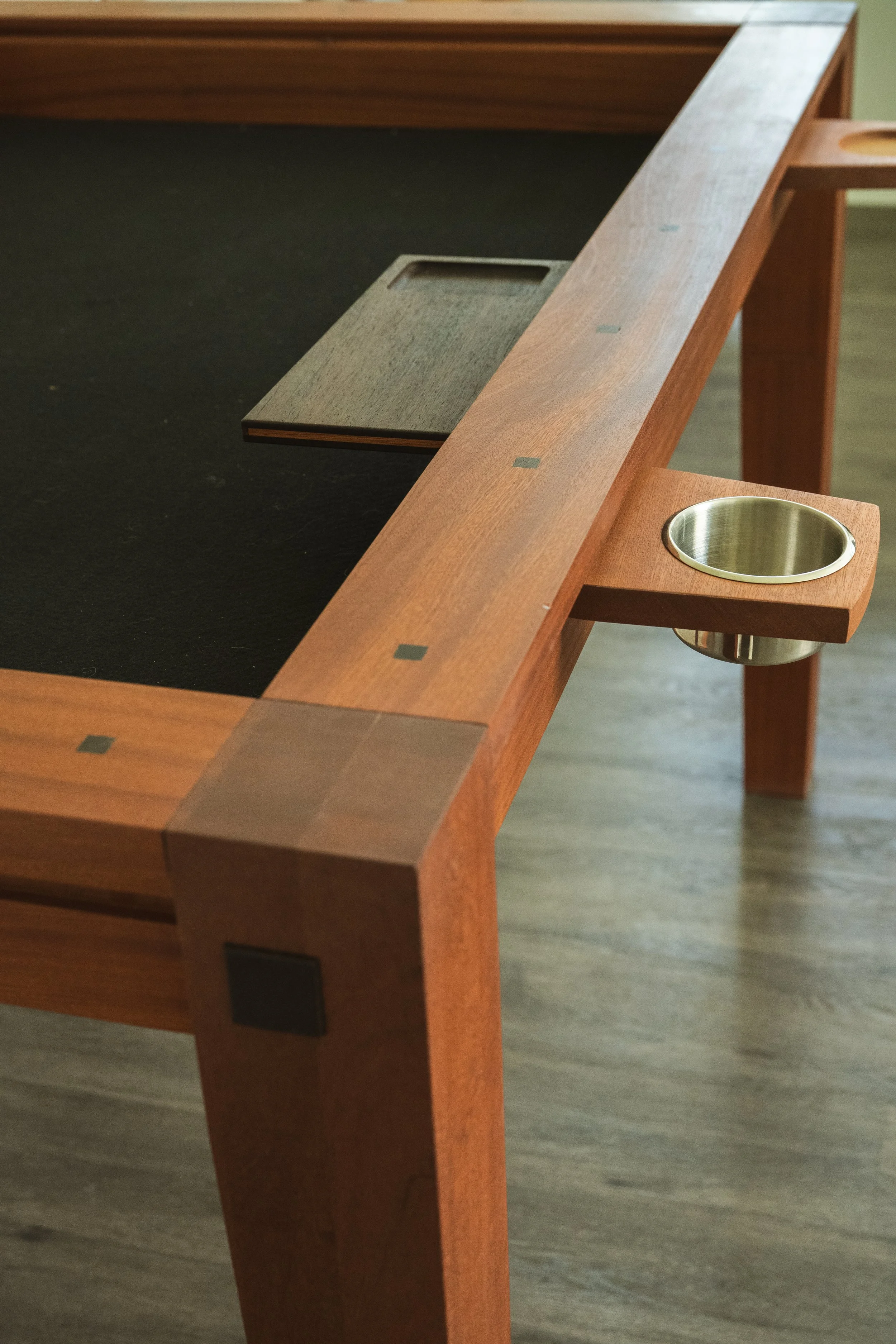 A wooden table with a built-in hot plate, a metallic cup holder, and a rectangular dish on top, positioned on a wooden floor.