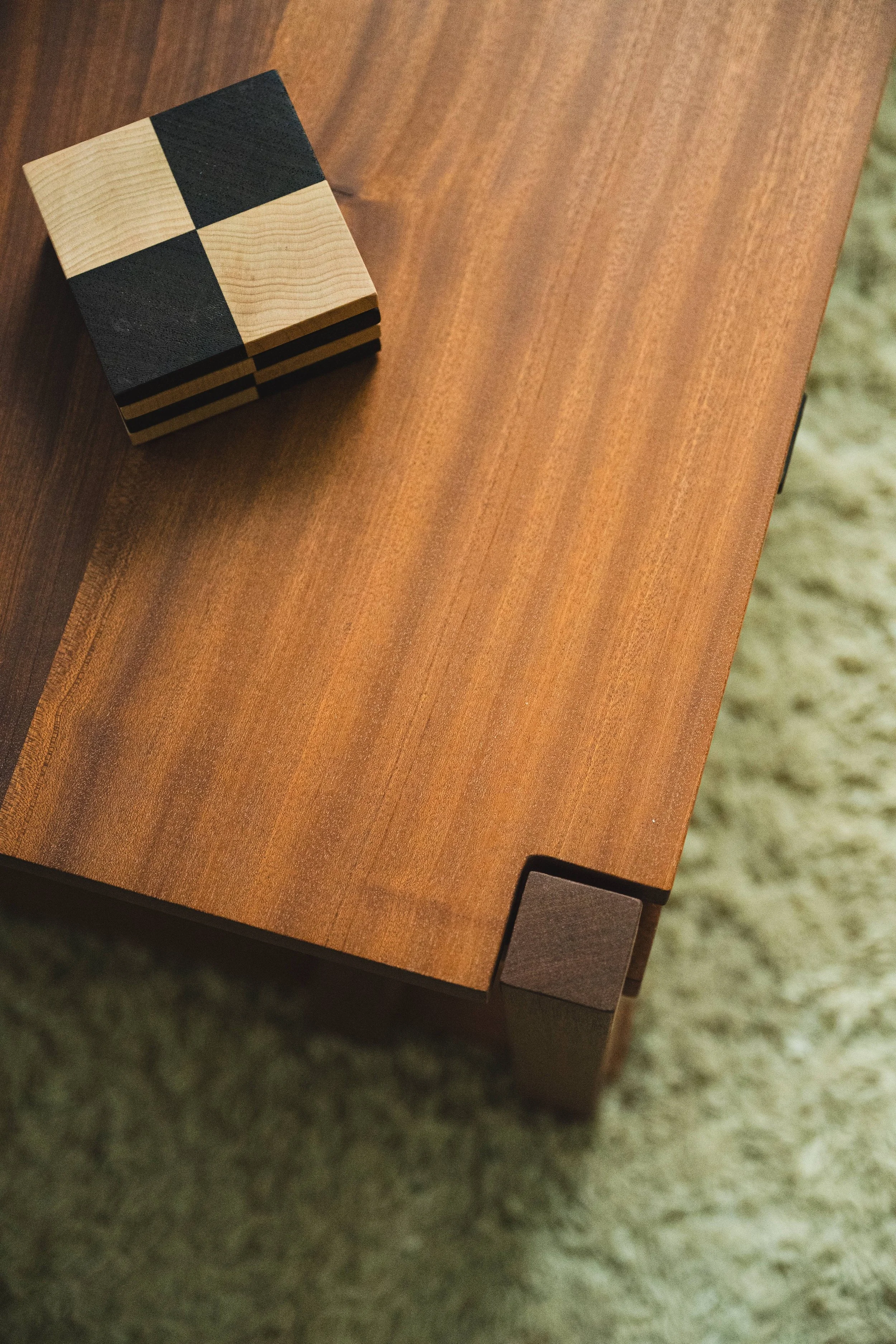 A wooden table with a black and light wood checkered cube resting on it, with a textured rug underneath.