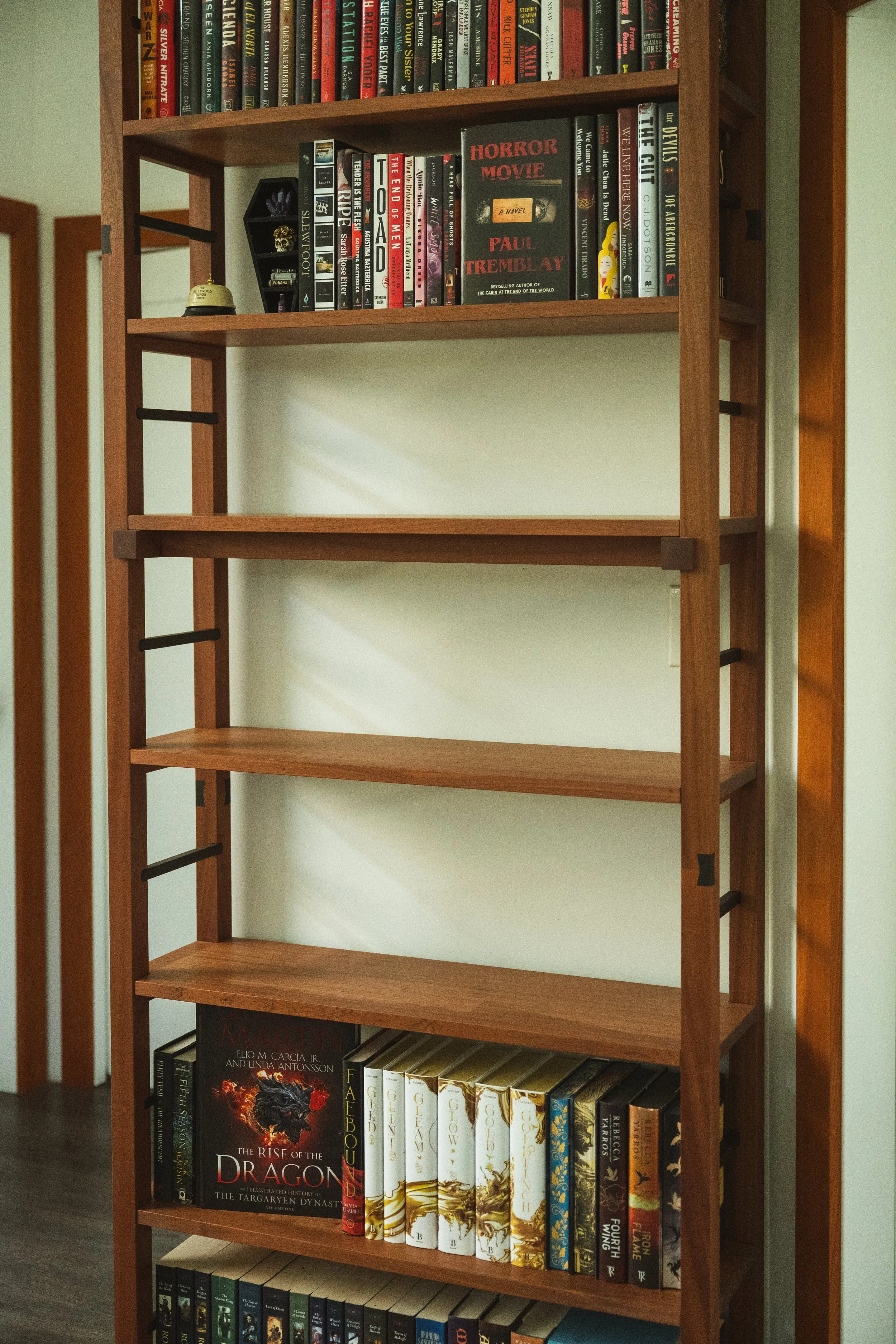 A wooden bookshelf with three shelves, filled with books.