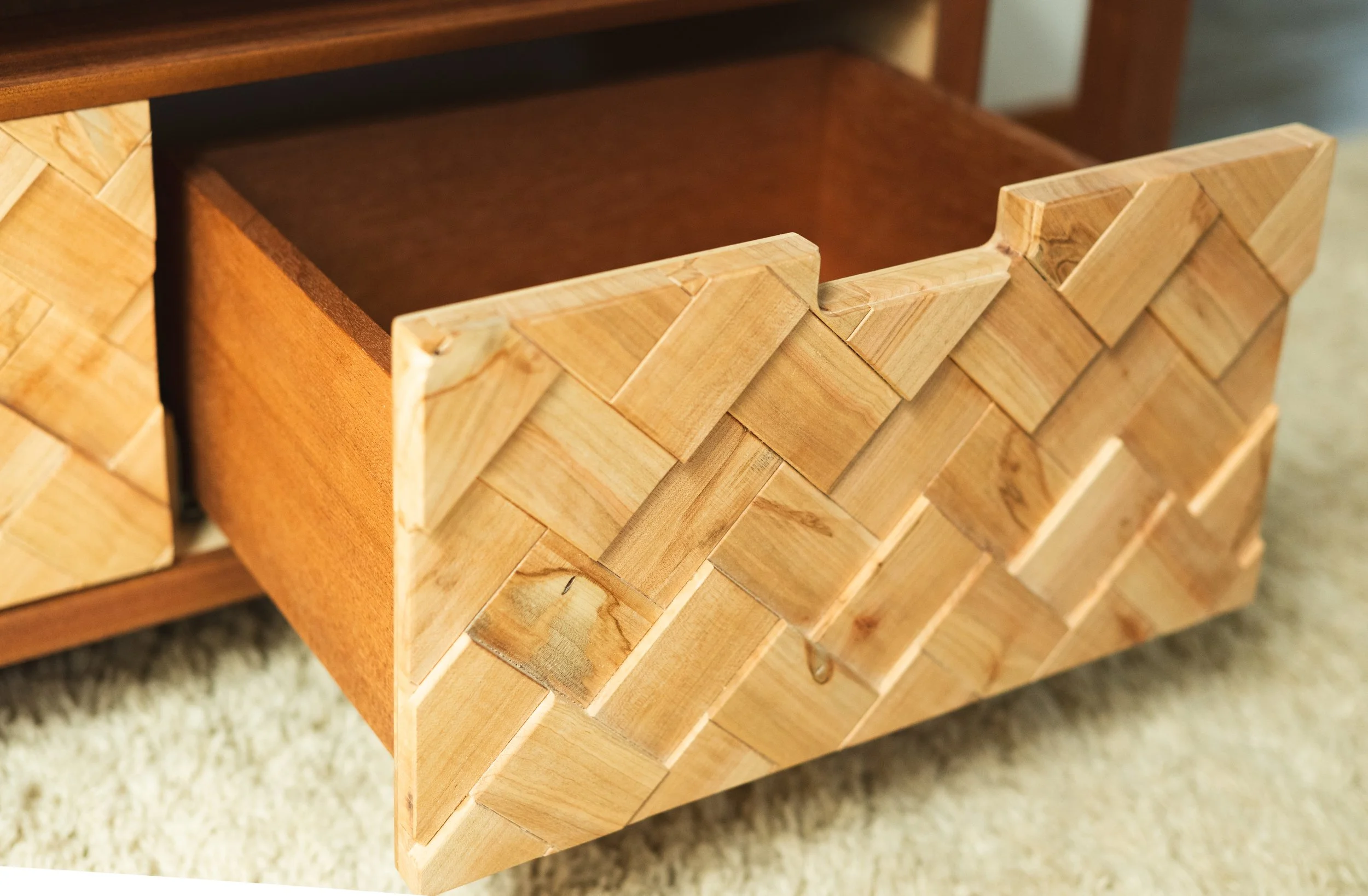 Close-up of a woven wooden basket with an open top, placed on a beige carpeted floor.