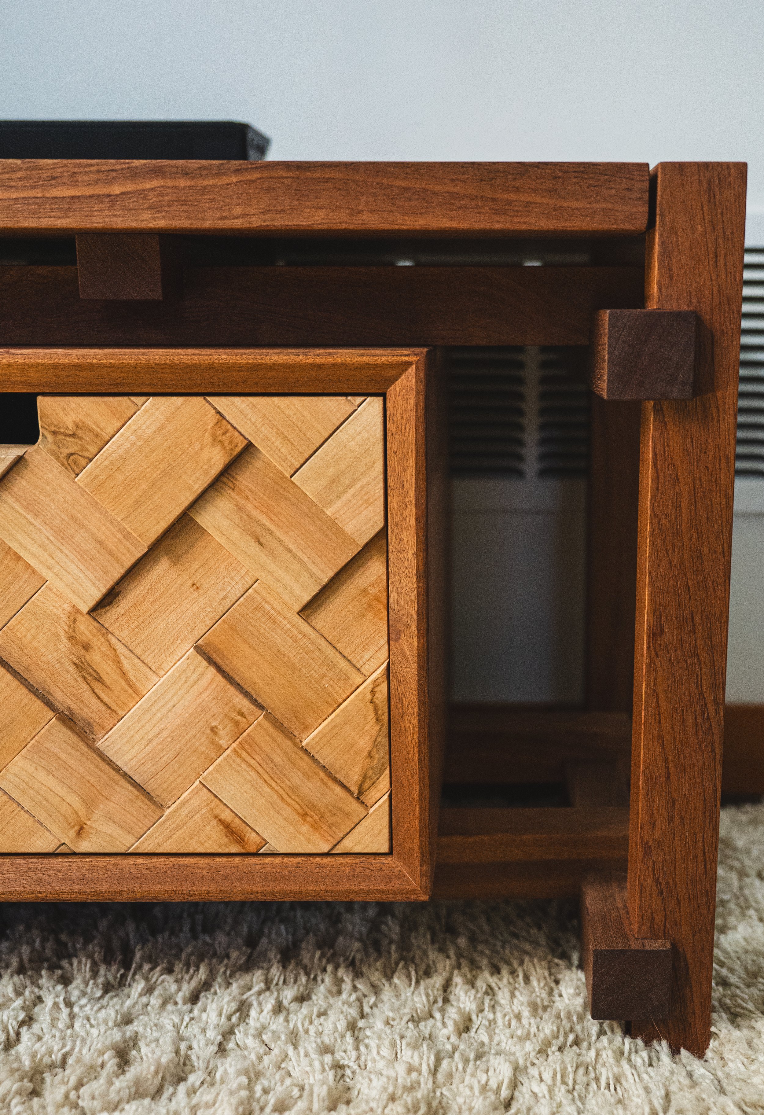 Close-up of a wooden cabinet with a woven pattern on the door, sitting on a plush beige carpet.