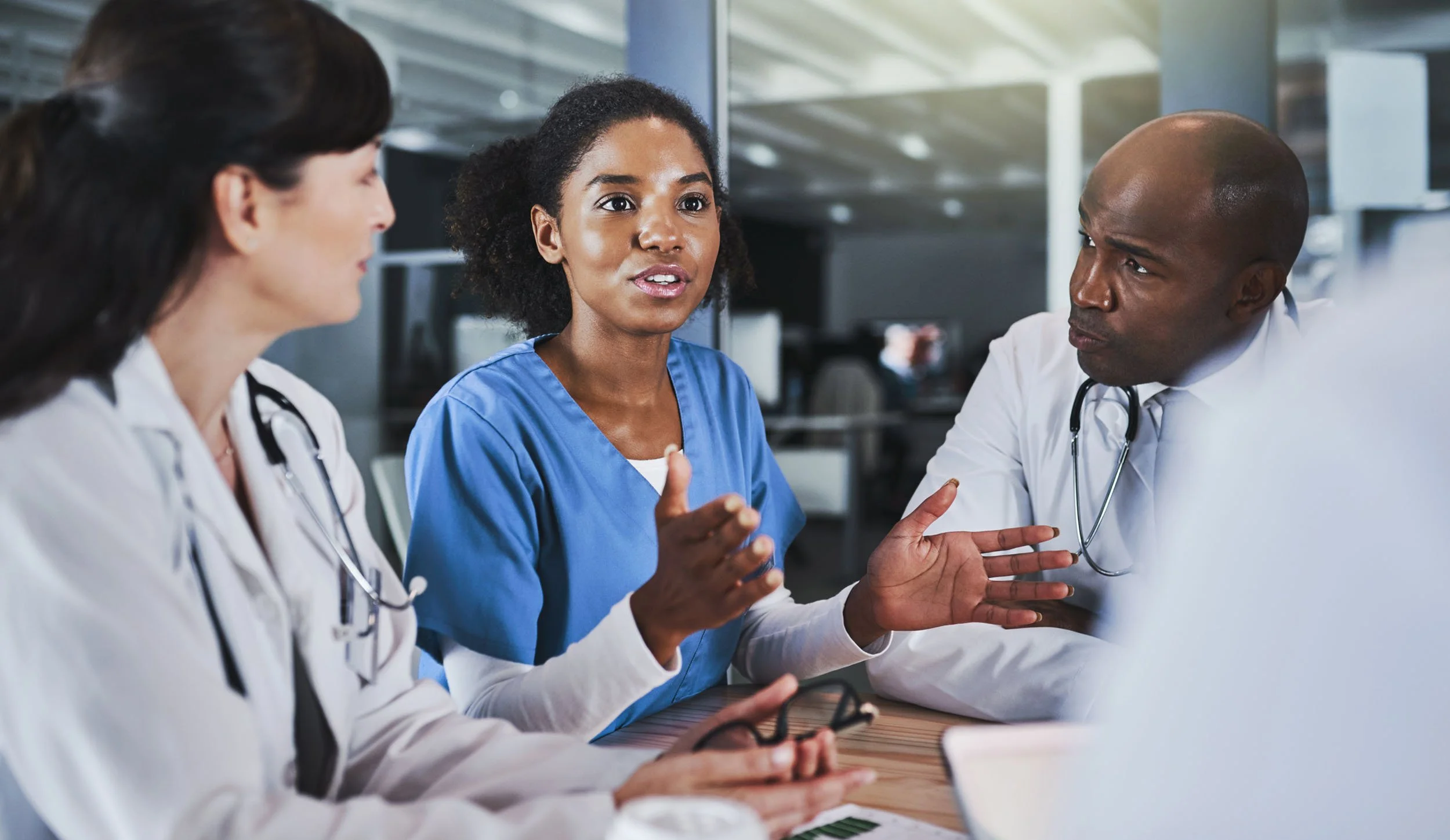 Healthcare professionals collaborating during a clinical discussion, with doctors and a nurse reviewing patient care together in a modern hospital setting.