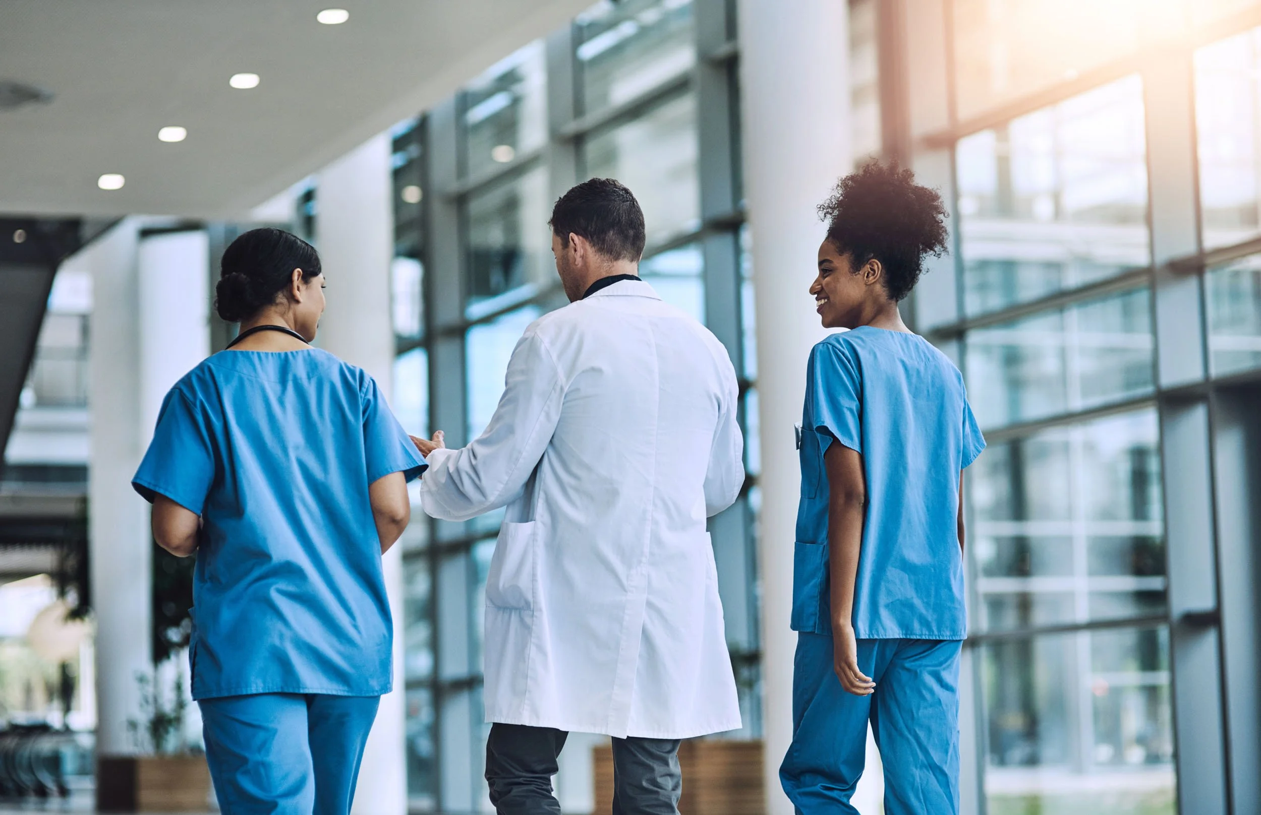 Doctor and two nurses walking through a modern hospital corridor while discussing patient care and collaborating as a healthcare team.