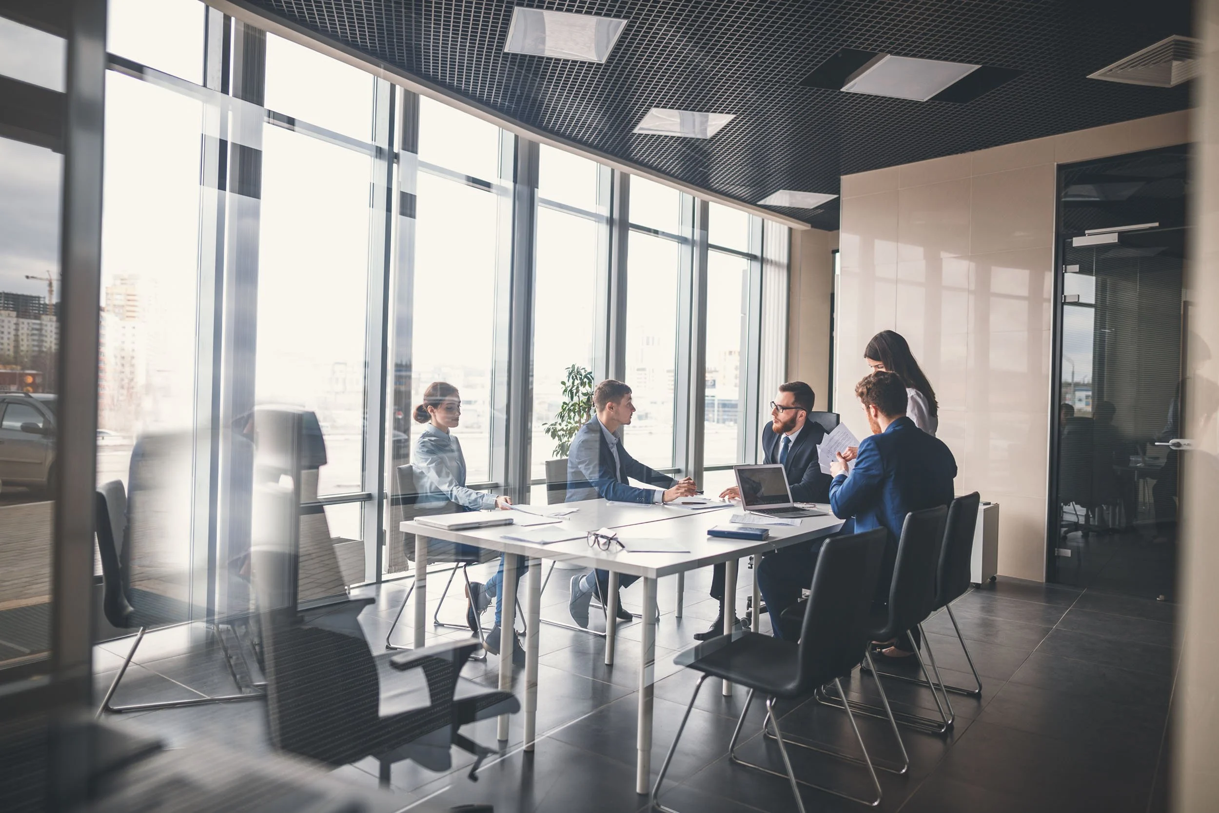 Business professionals meeting in a modern conference room, discussing strategy and collaborating around a table with laptops and documents.