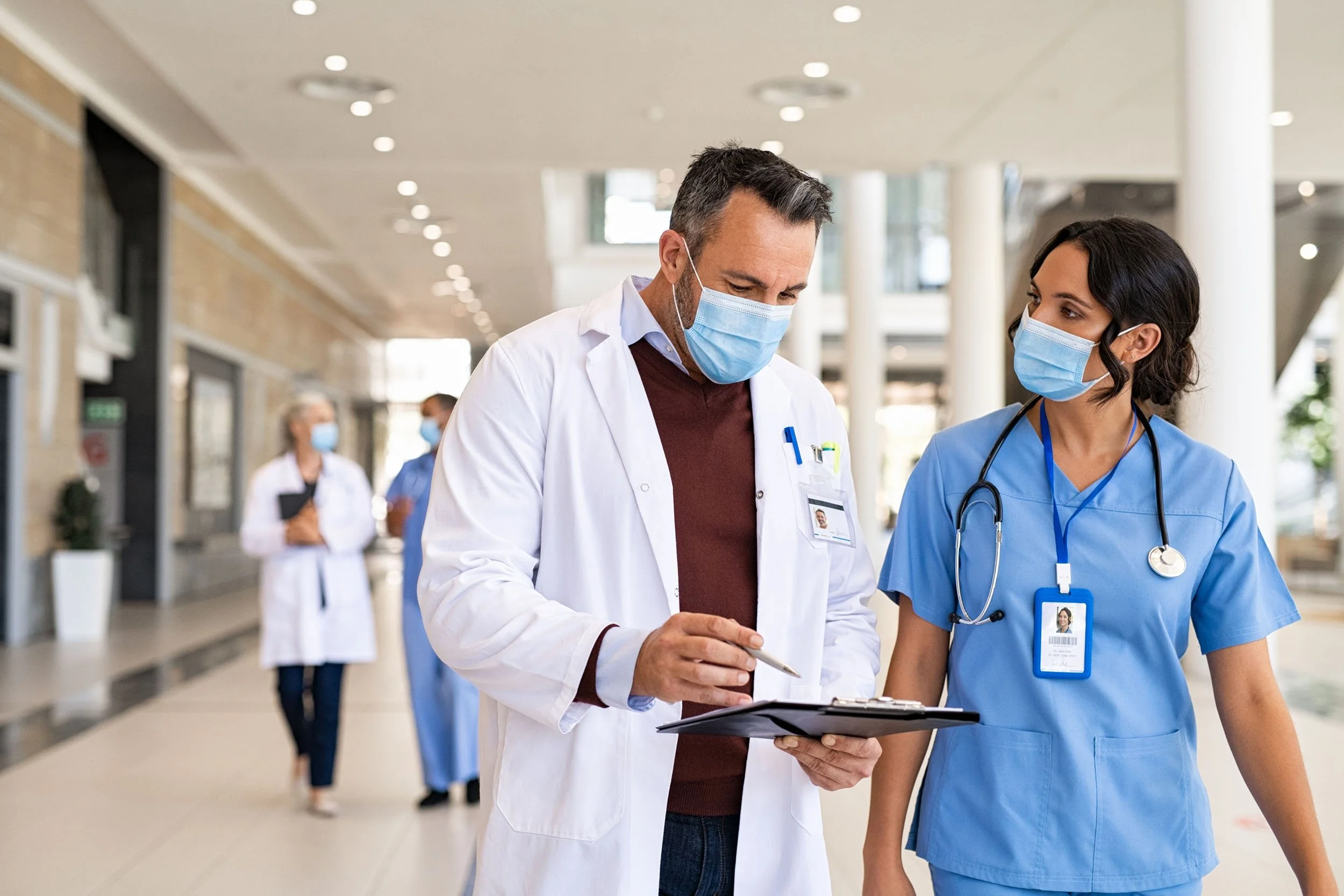 Doctor and nurse reviewing patient information on a clipboard while walking through a hospital corridor, collaborating on patient care in a modern healthcare facility.