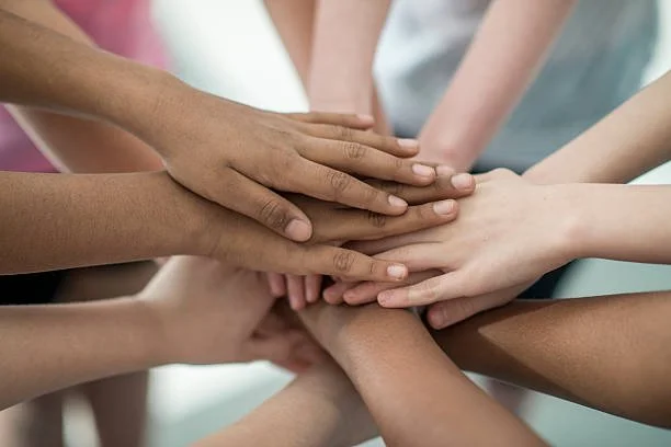 Multiple hands of diverse individuals stacked together in a gesture of unity.