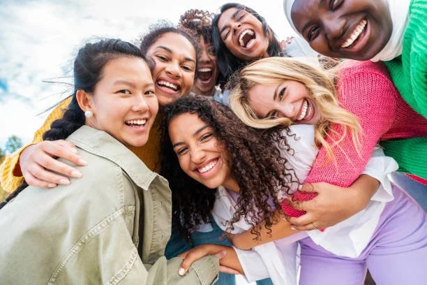 Group of diverse women smiling and hugging each other outdoors.