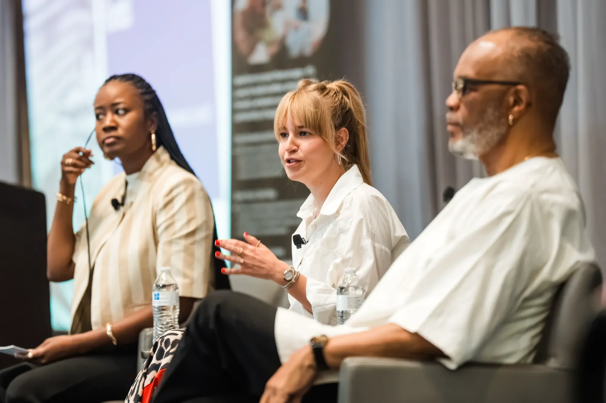 Three diverse people seated at a panel discussion. The woman in the middle is speaking.
