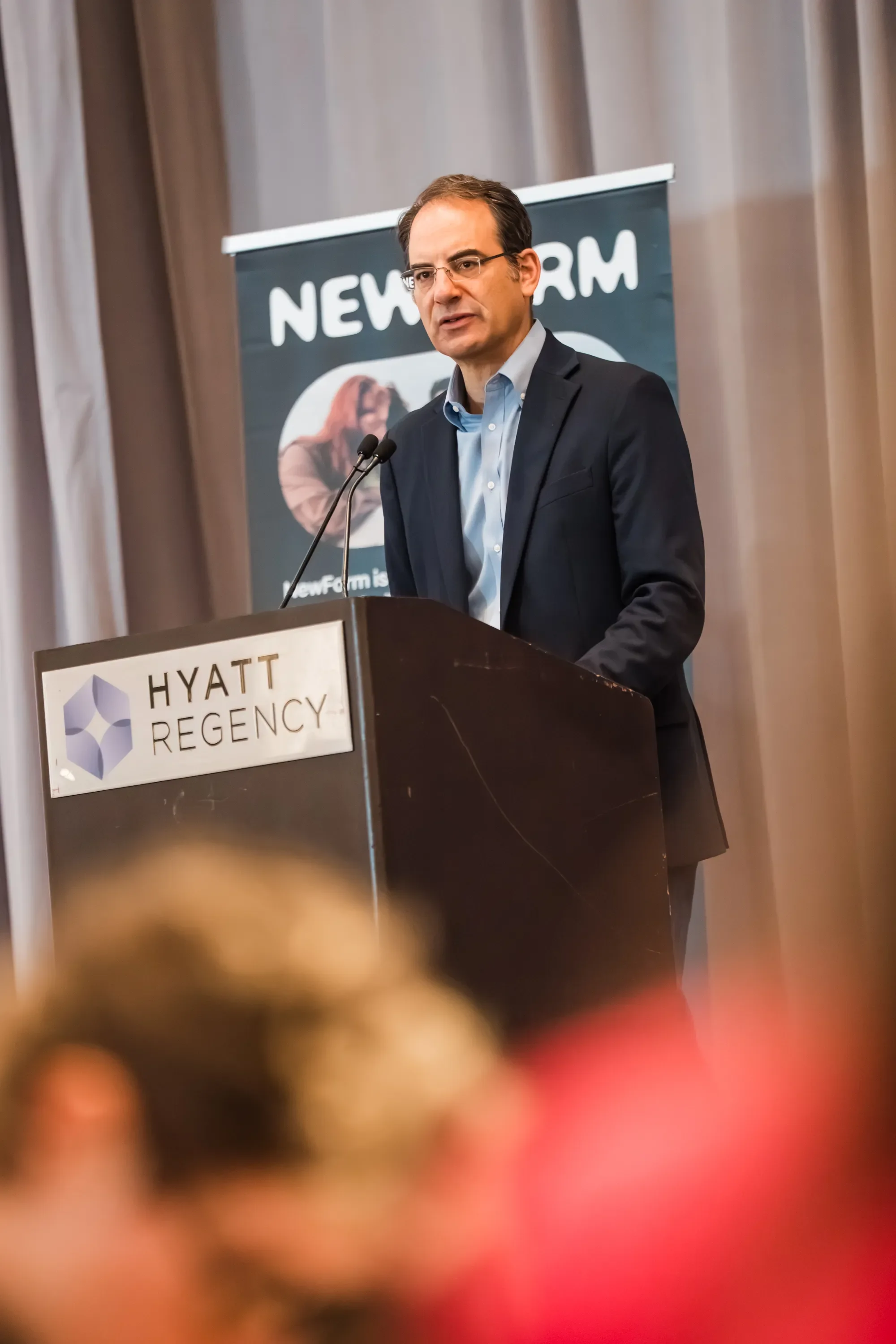 A man in a suit speaking at a podium during a conference at the Hyatt Regency hotel.