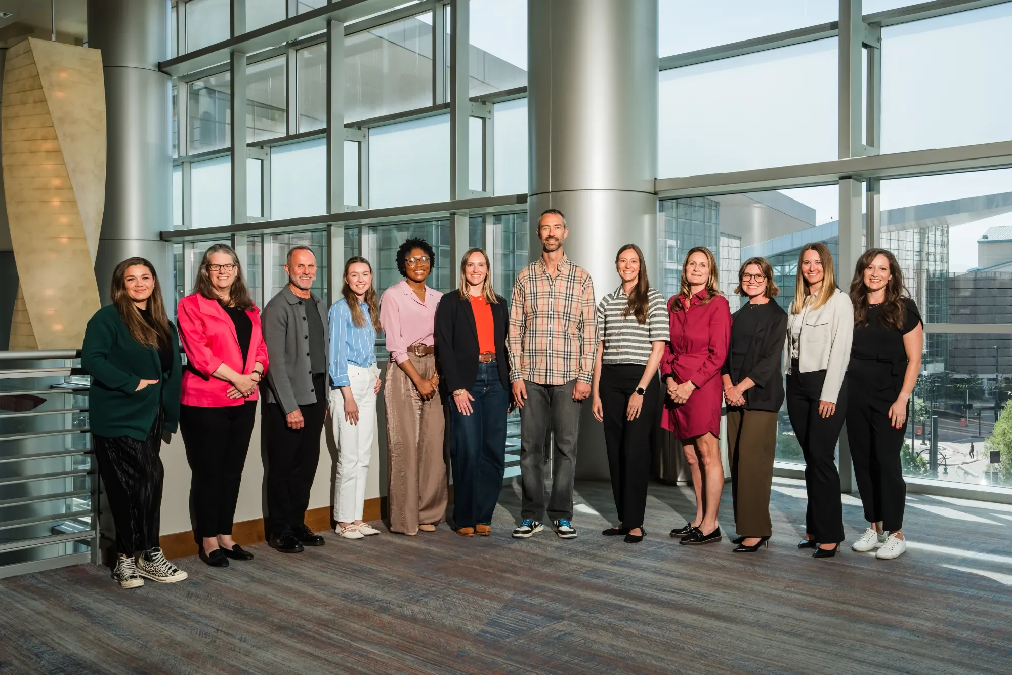 NOSC team standing indoors in front of large glass windows, smiling and posing for a photo.