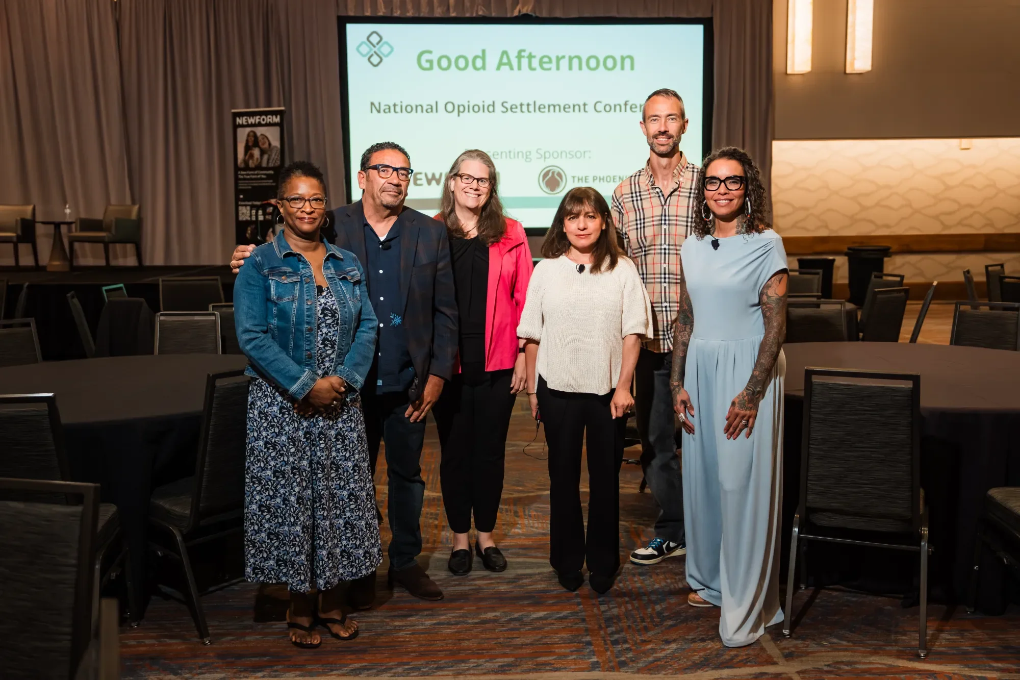 NOSC team standing together in front of a conference screen at a formal event, smiling at the camera.