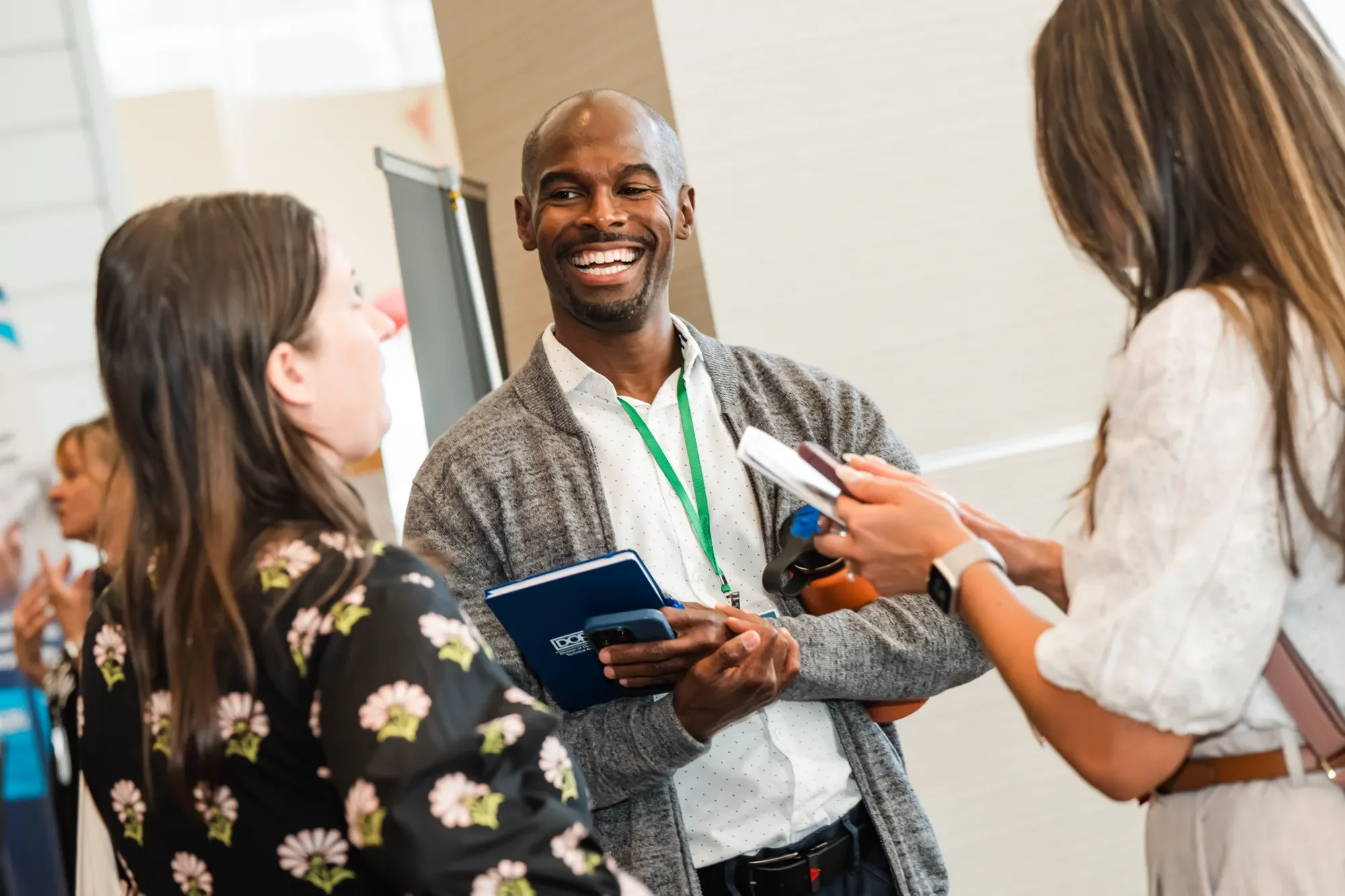 A man smiling as he talks to two women at what appears to be a conference or networking event.