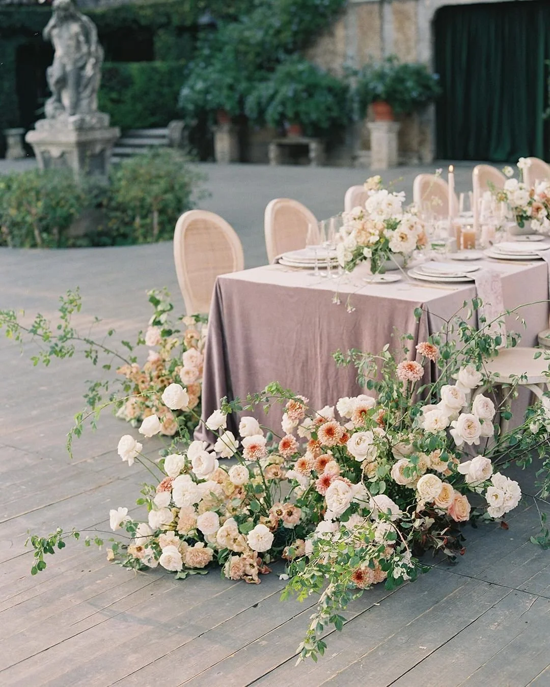 Elegant outdoor Simcoe-Muskoka wedding harvest style  table setting with floral arrangements, candles, and pastel-colored tableware on a mauve tablecloth, surrounded by greenery and pillar candles.