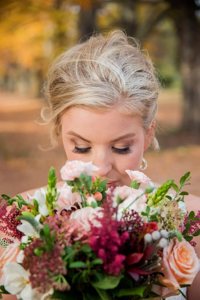 A happy bride with blonde styled hair smelling the fresh flowers of her fall wedding bouquet in Simcoe-Muskoka.
