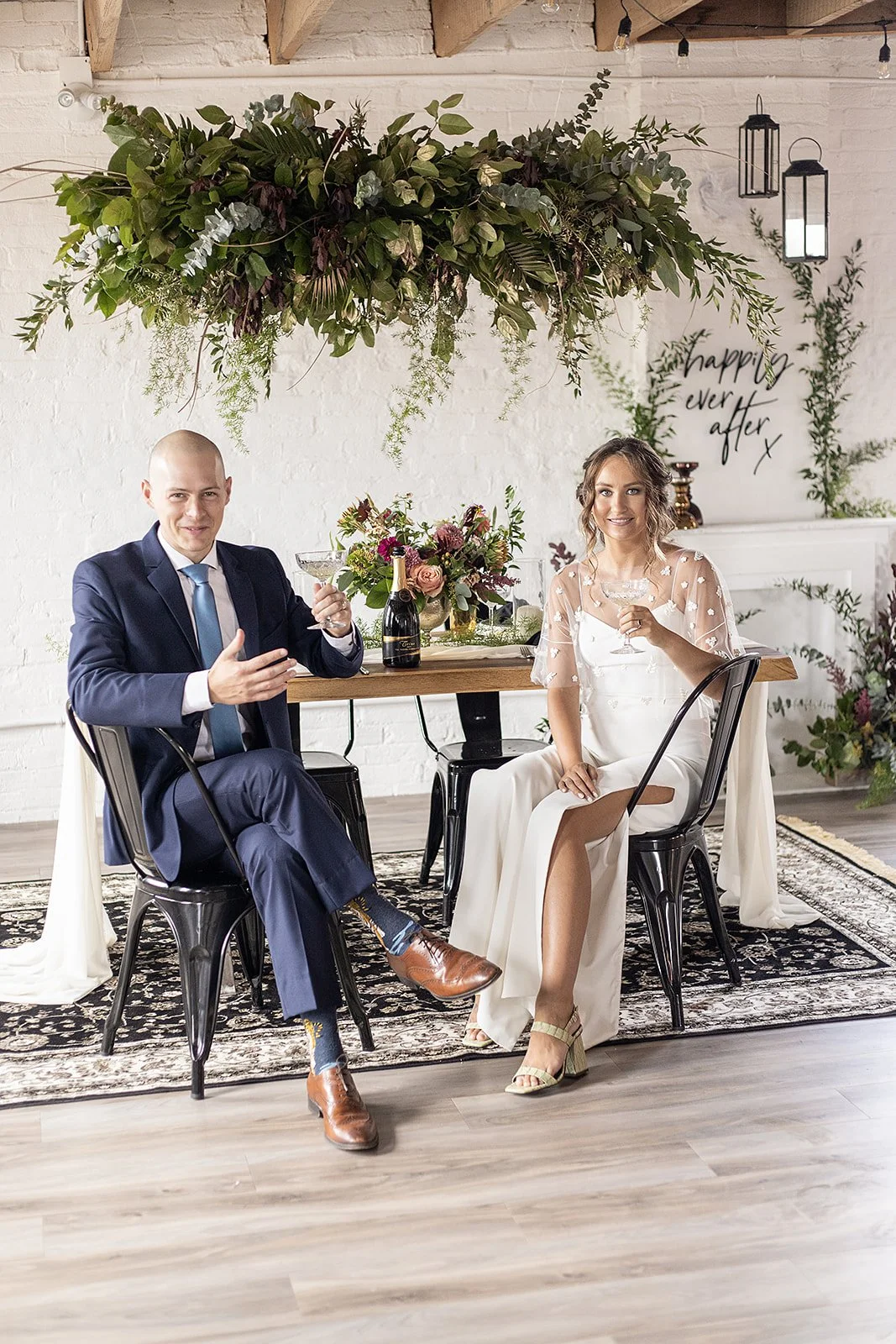 A man in a blue suit and a woman in a white dress sitting at a table with drinks celebrating their Georgian Bay Wedding Day.