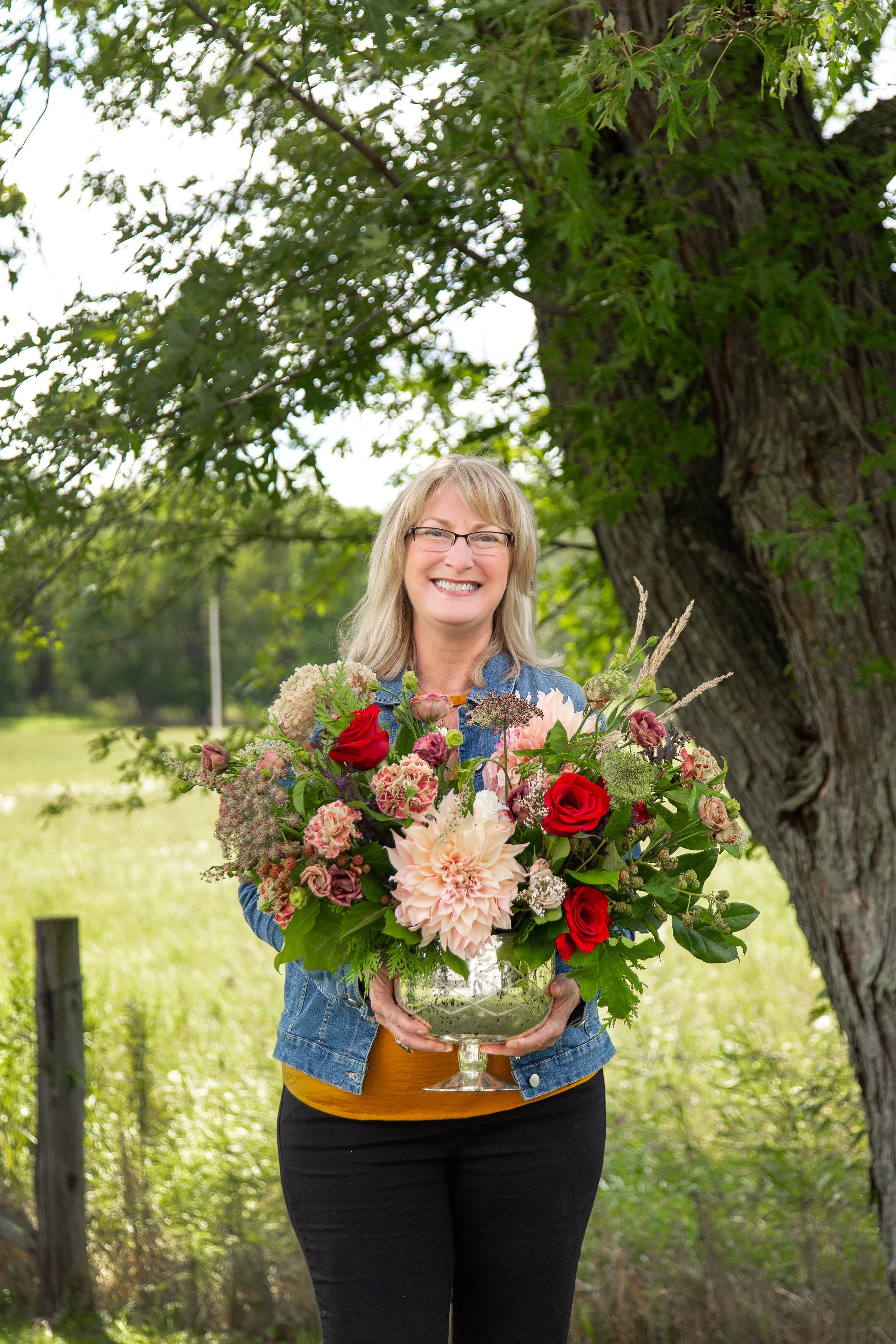 Florist holding a gold vase of flowers standing by a tall tree