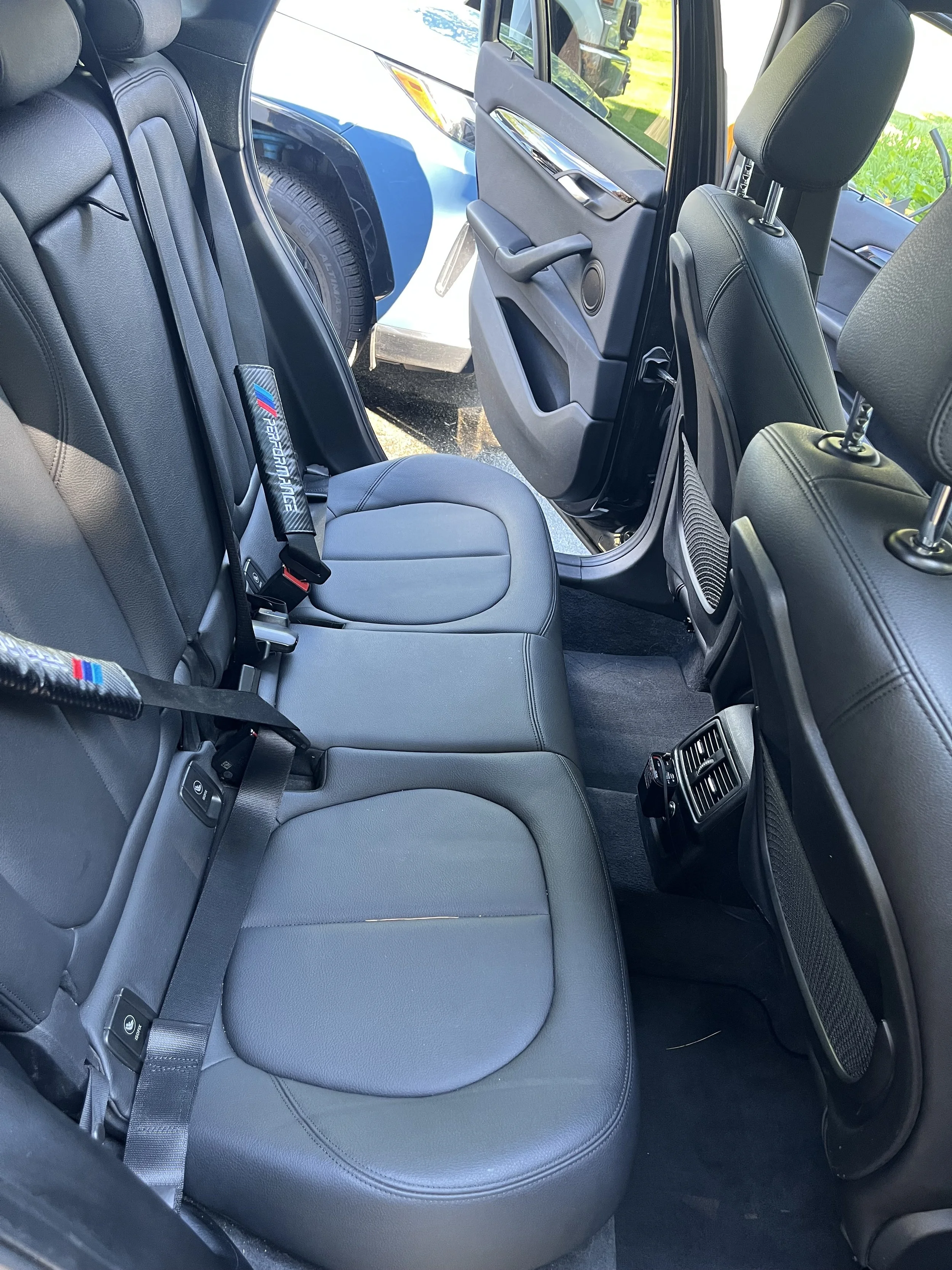 The interior of a vehicle showing the back seats with black leather upholstery, and the front passenger seat. The side door and window are open.