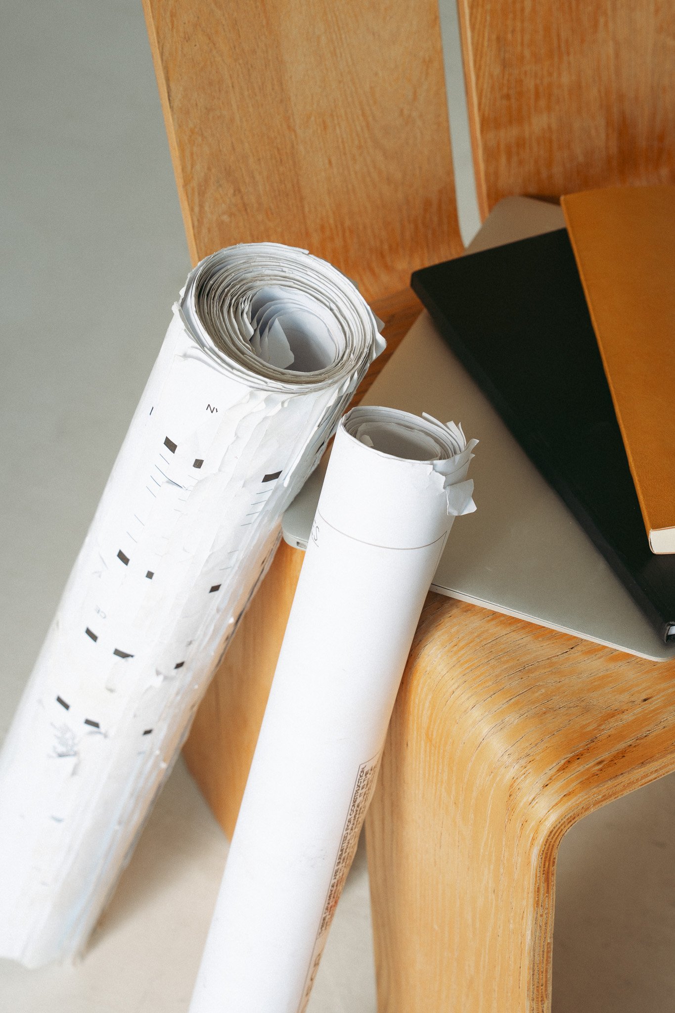 Two rolled-up sheets of paper on a wooden table with a black object and a book nearby.