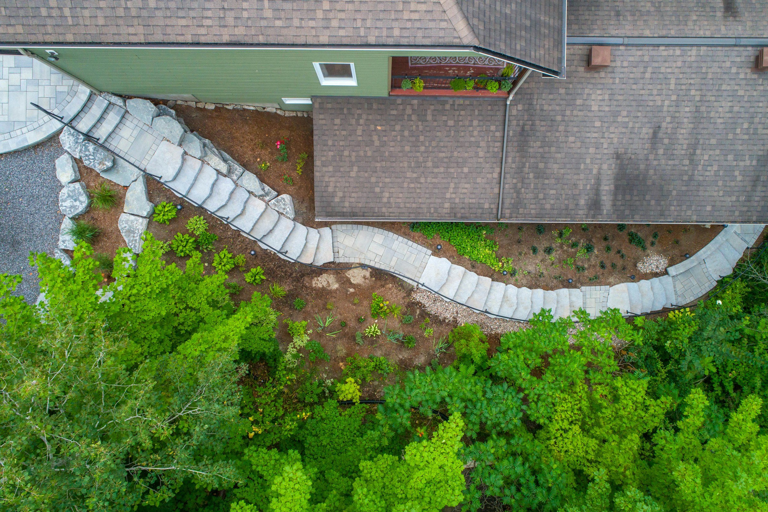 Aerial view of a backyard with a green house, stone stairs, a garden bed, and trees.