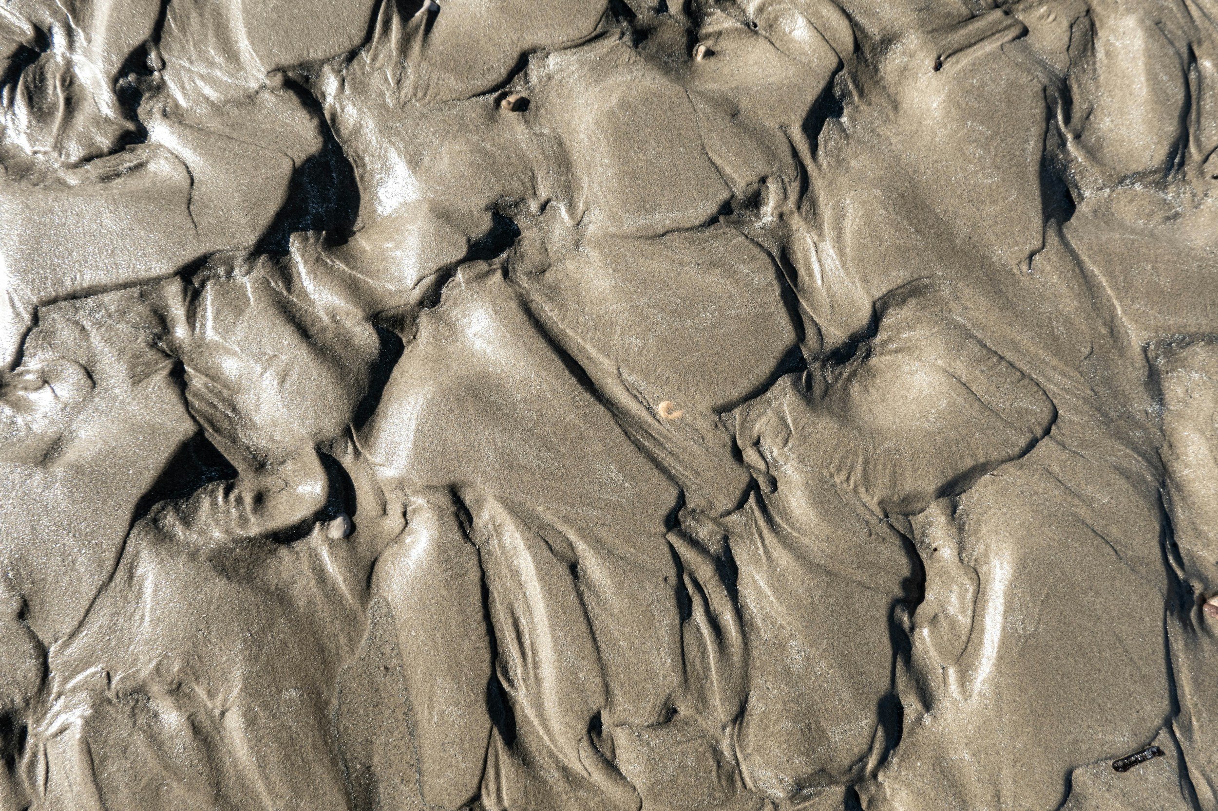 Close-up of wet, textured sand with various cracks and ridges