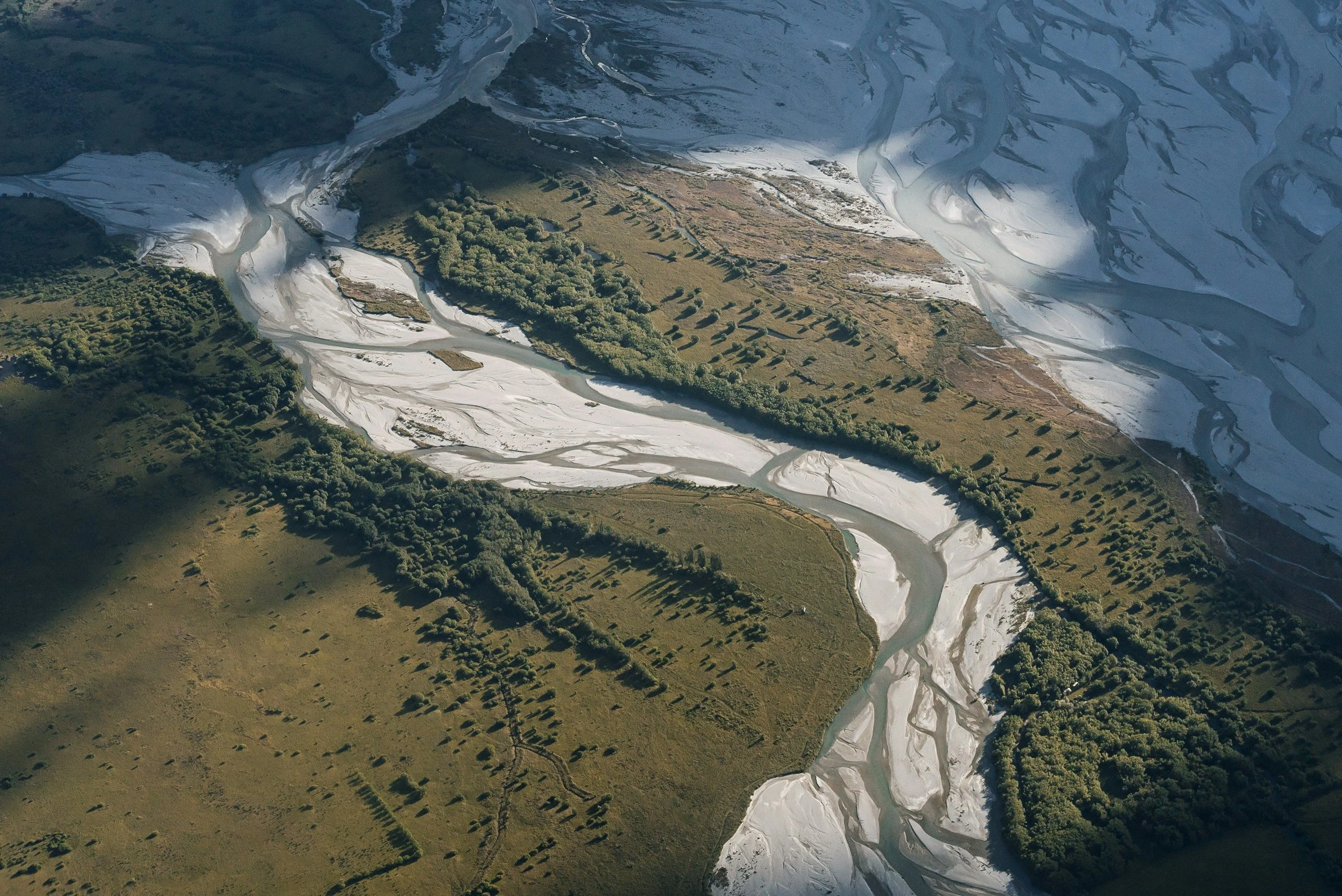 Aerial view of a river flowing through a landscape with green vegetation and snow-covered areas.