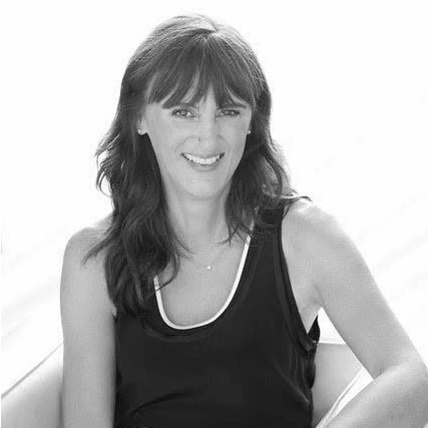 Black and white photo of a woman with long wavy dark hair, smiling and wearing a sleeveless top with a white trim.
