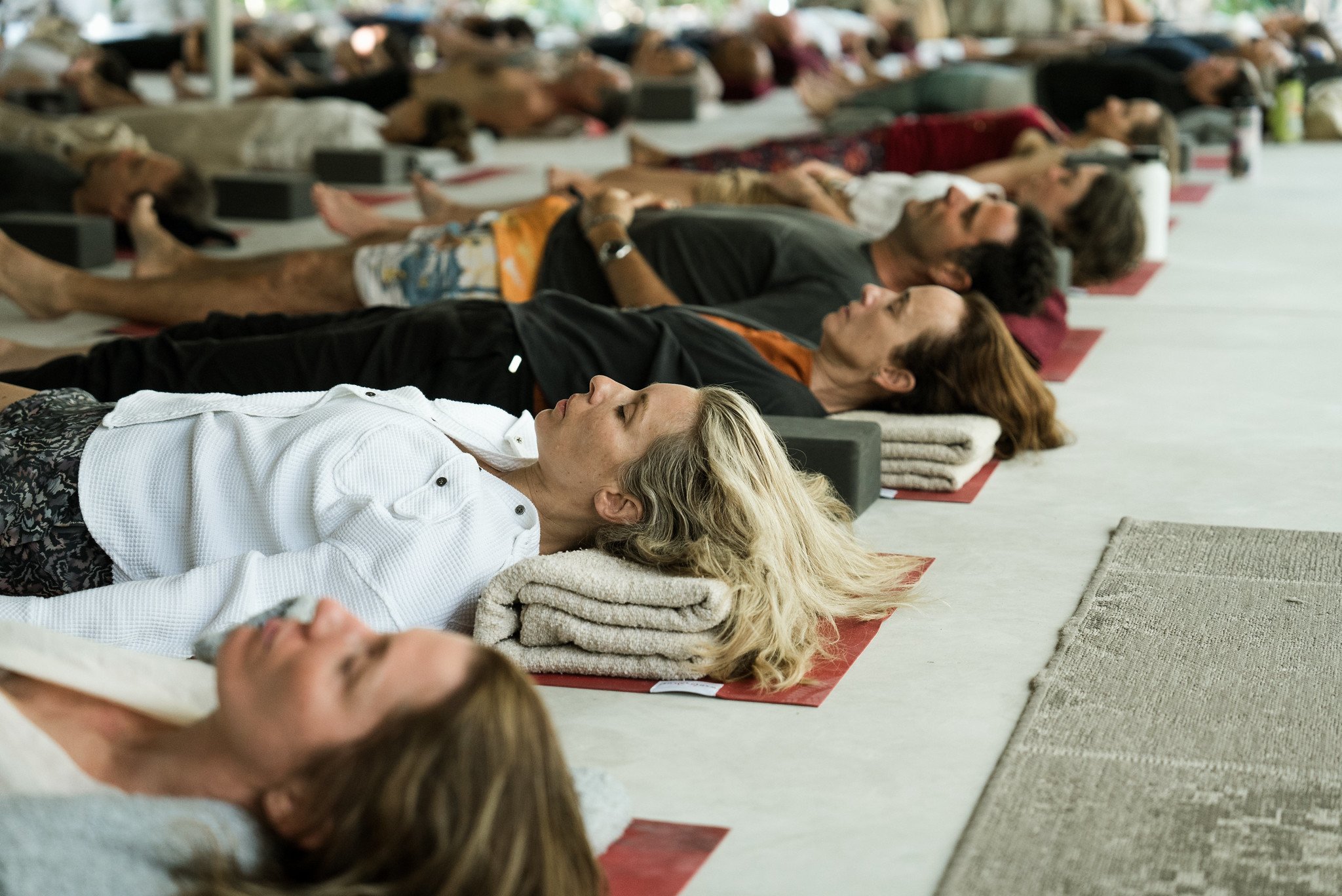 People lying on mats with blankets, practicing yoga or meditation in a large indoor space.