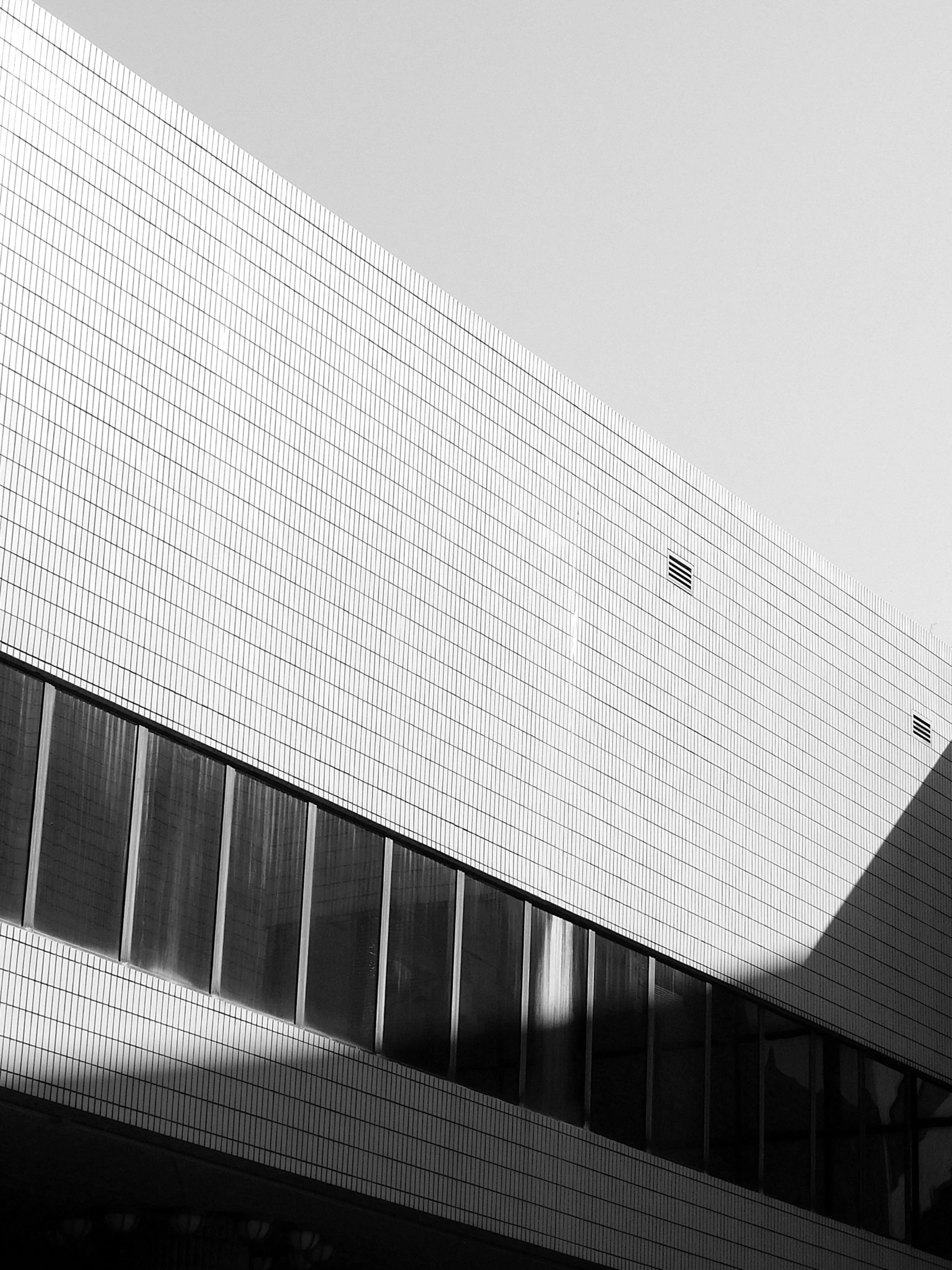 A modern multi-story building with a grid-patterned facade and large glass windows, viewed from an angle. The building is mostly white with a minimalist architectural style.