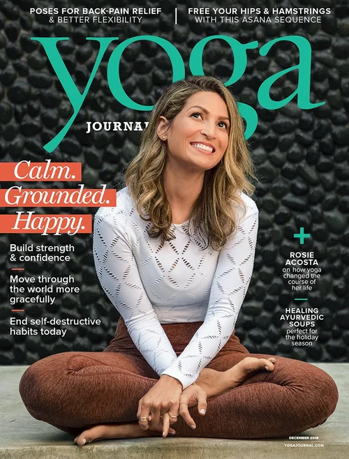 Rosie Acosta seated on a yoga mat on the cover of Yoga Journal, December 2018