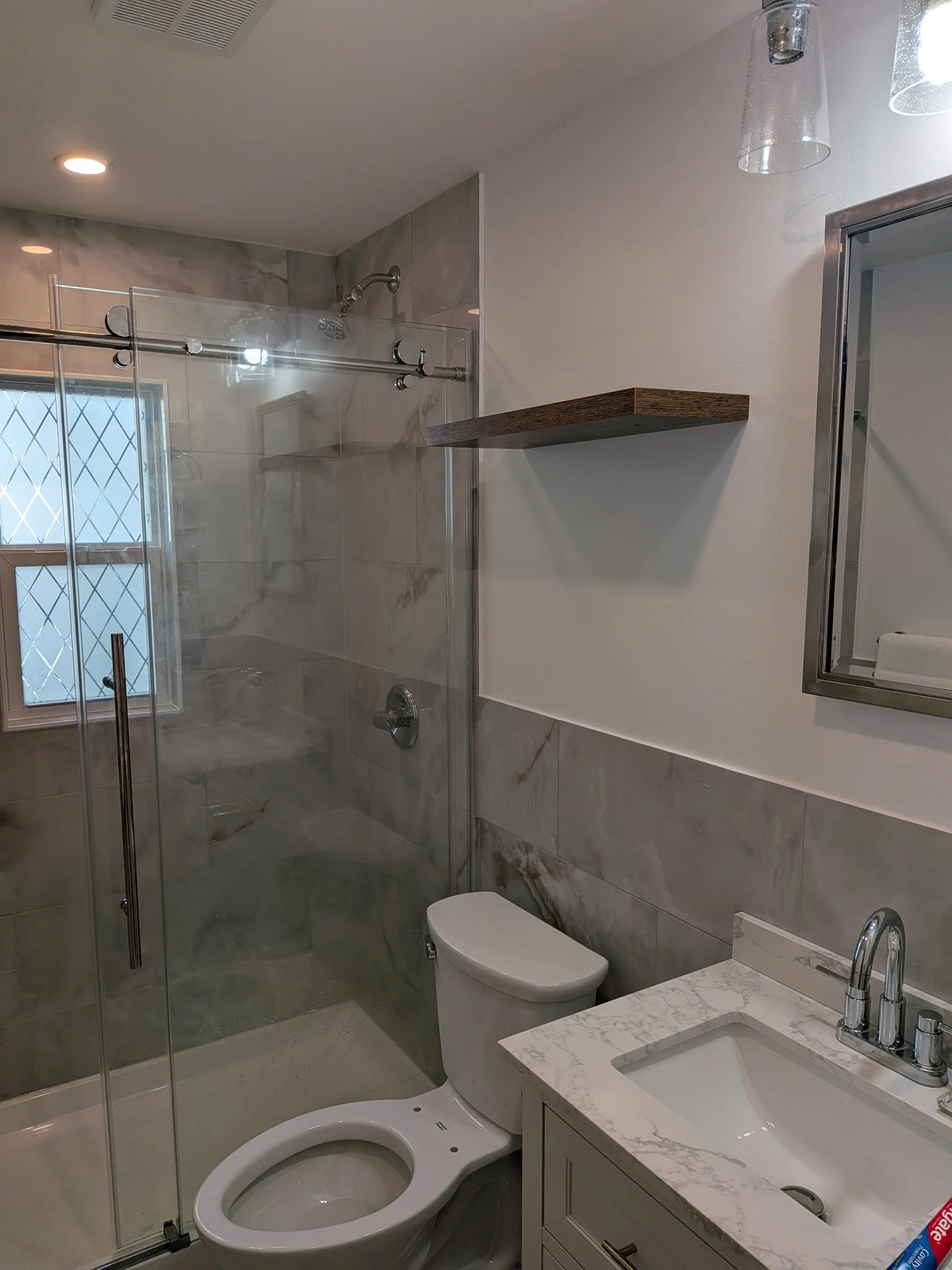 Modern bathroom remodel with 12"x24" tile and glass shower doors.