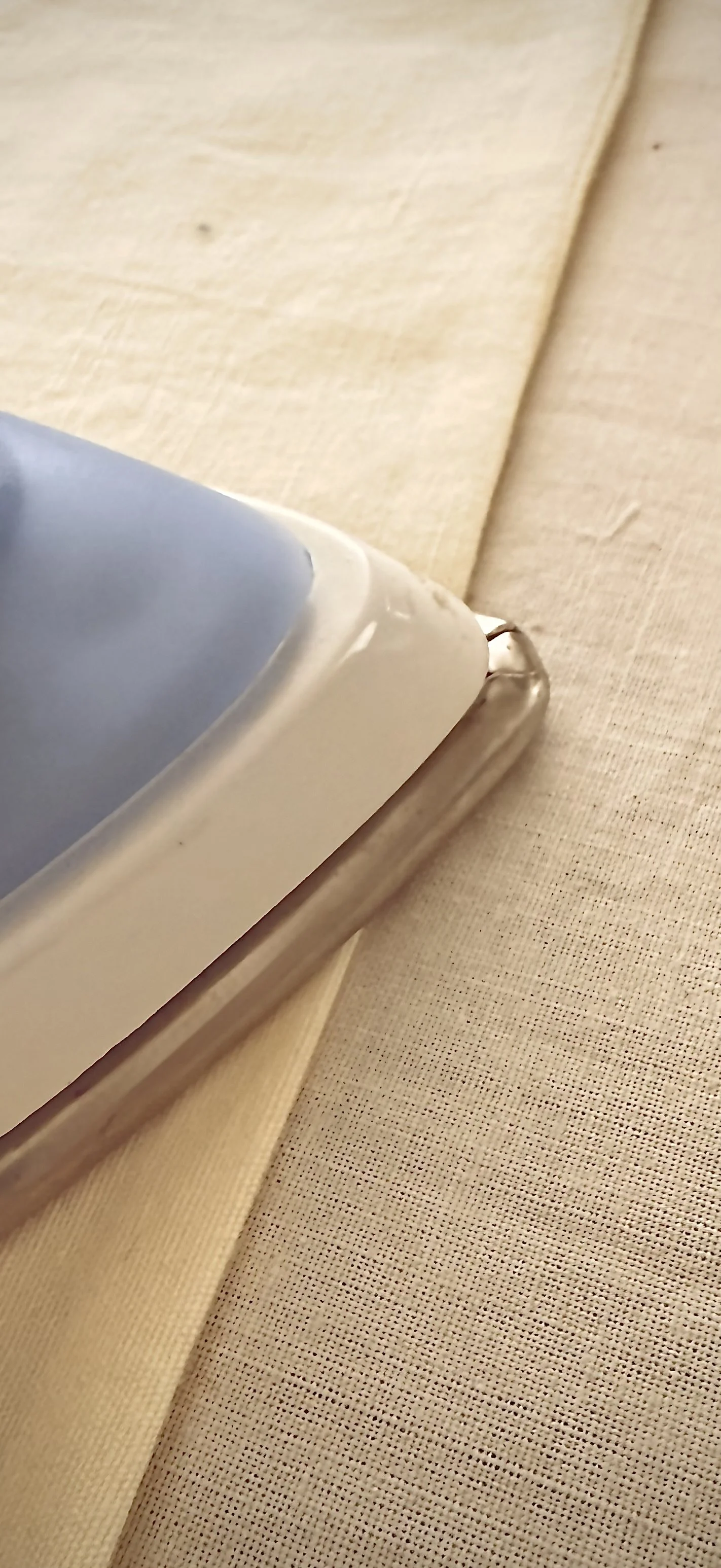 Close-up of a corner of a white fabric being ironed on a beige textured surface.