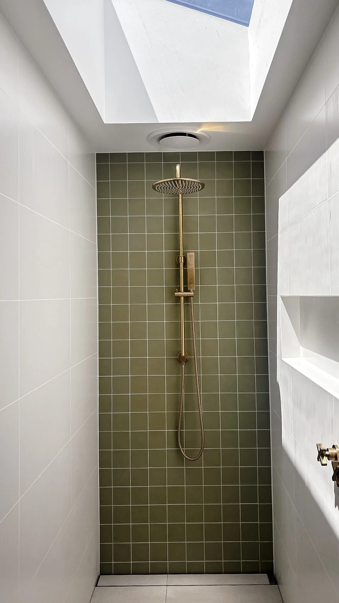 Shower with green tiled wall, brass showerhead, and overhead skylight.