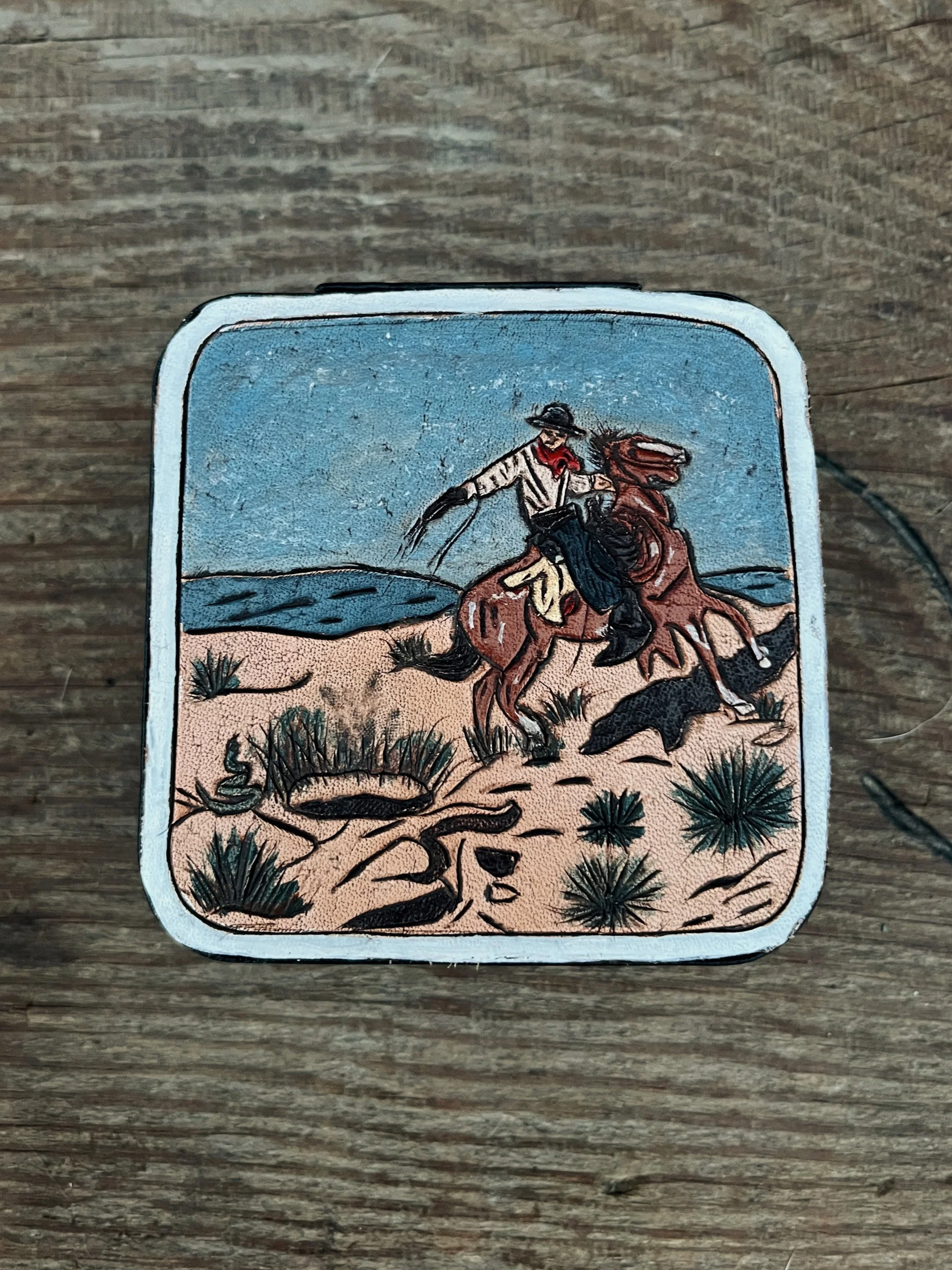 An illustration of a cowboy riding a bucking horse in a desert landscape with small bushes and distant mountains.