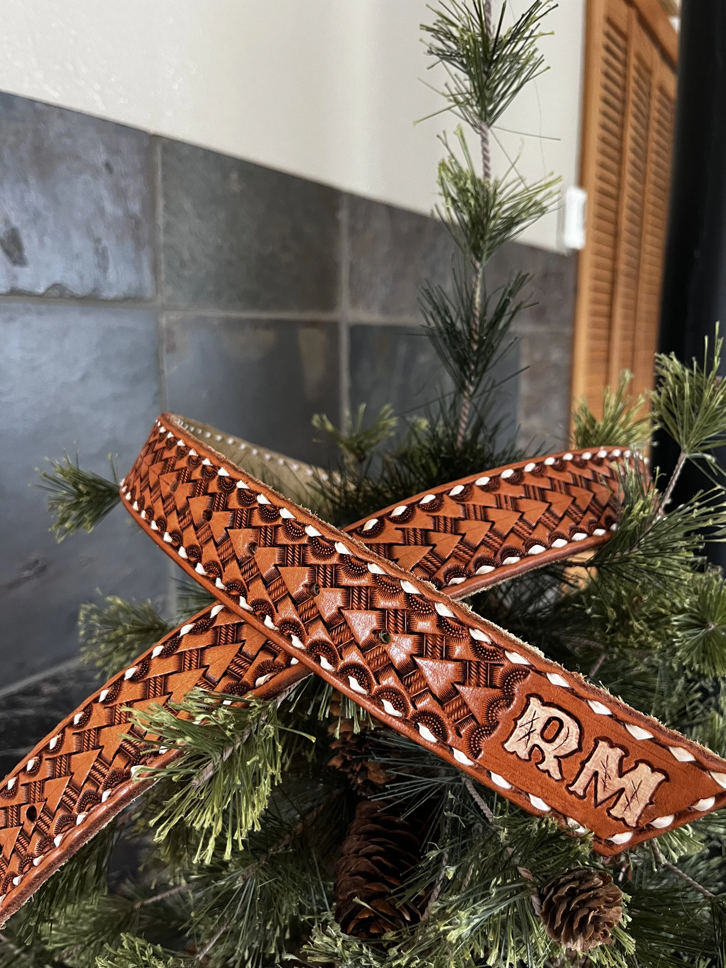 Close-up of a Christmas decoration featuring pine branches, pinecones, and orange ribbon with a decorative pattern, with text that reads "Merry Christmas".
