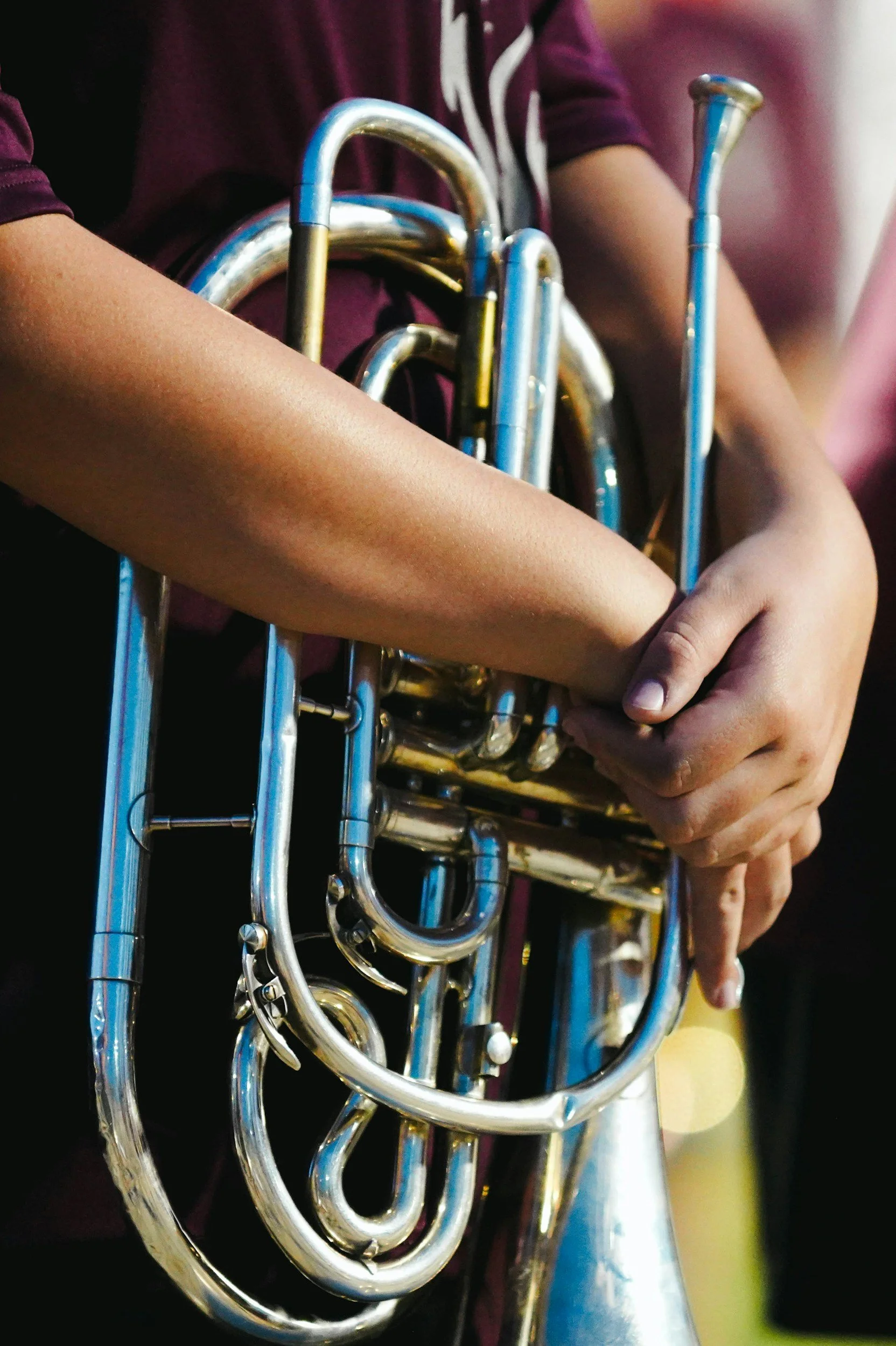 A person holding a silver trumpet, with another person in the background. The focus is on the trumpet and hands.