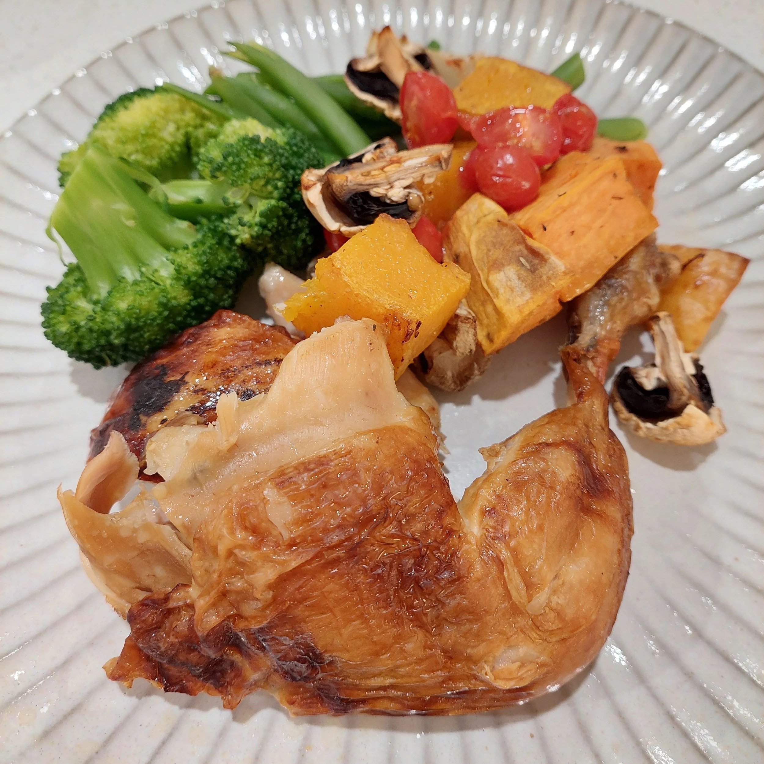 Roast chicken with roasted pumpkin, mushrooms, tomatoes, broccoli and green beans on a ribbed plate.