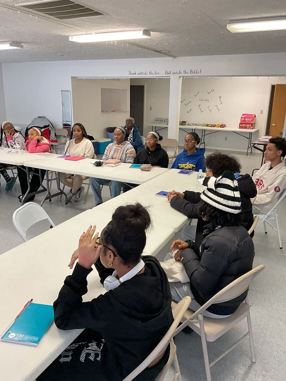 Group of young people seated at tables in a classroom or meeting space.