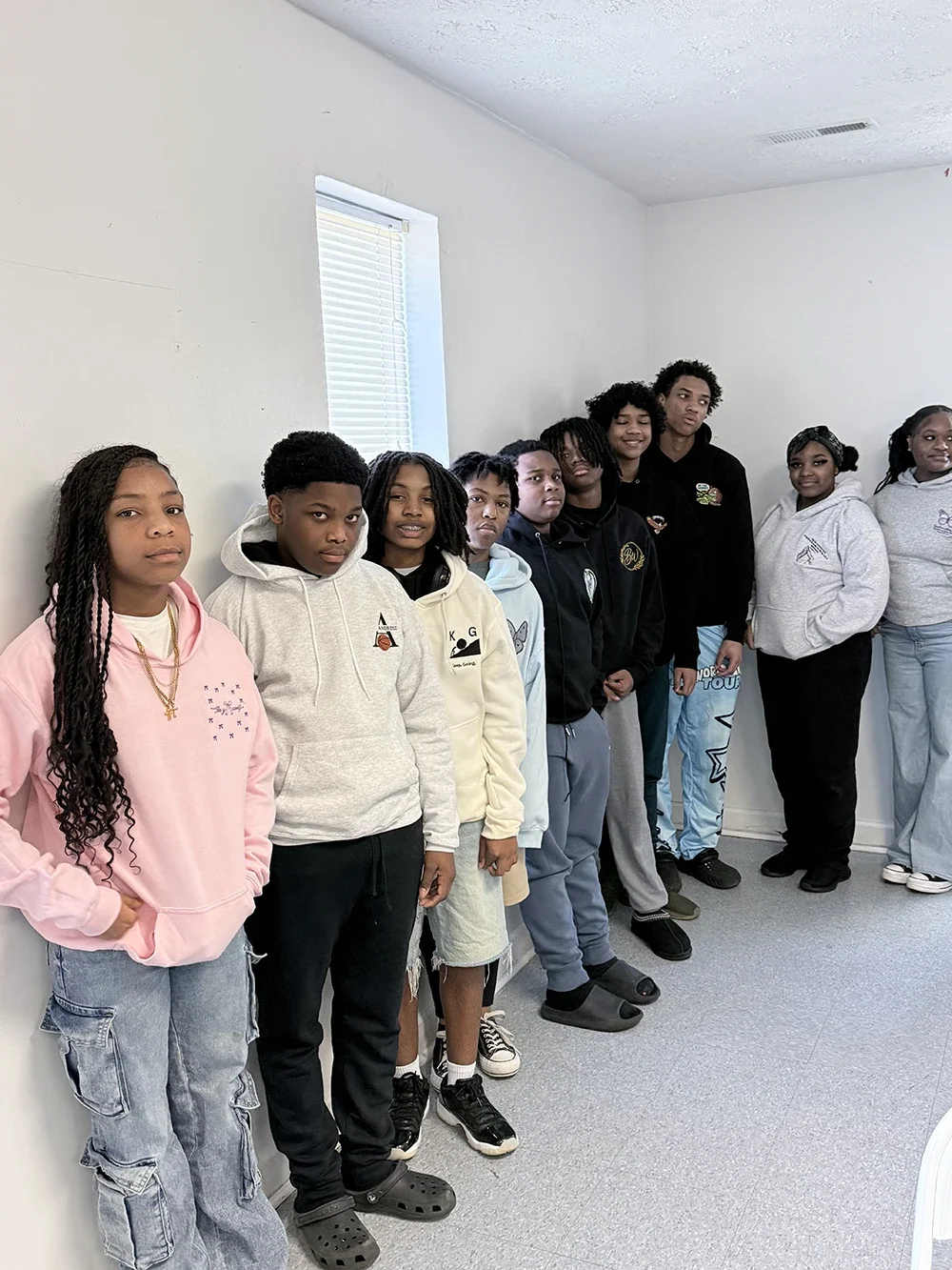 A group of young people standing against a white wall in a room.