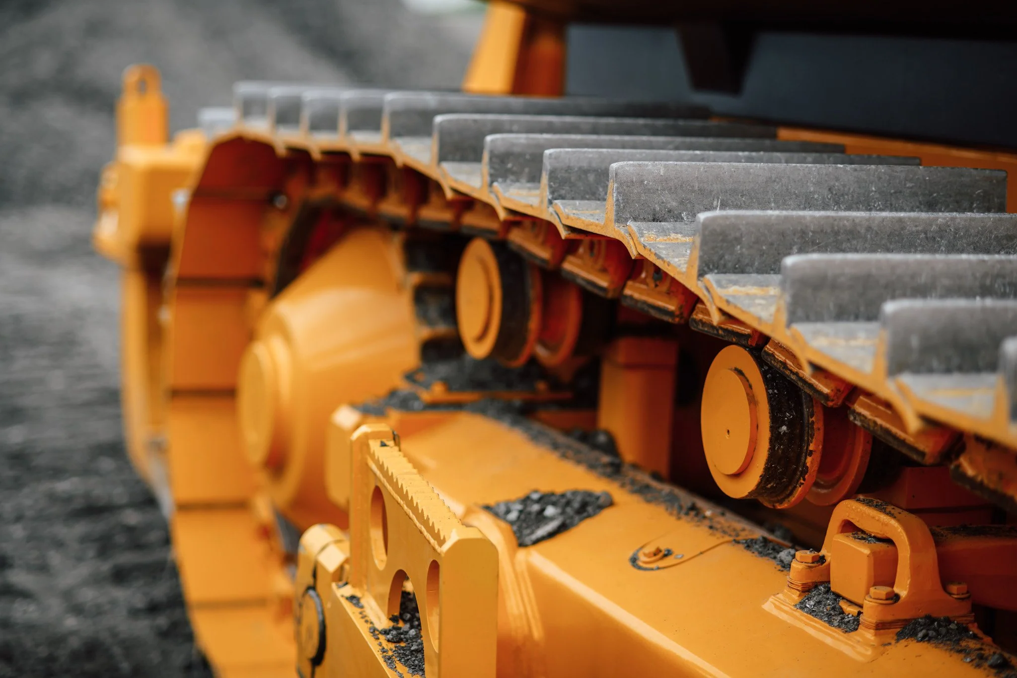 Hire Equipment Machine Western Australia South West WA - Close-up of an orange construction vehicle track with metal treads on dirt ground.