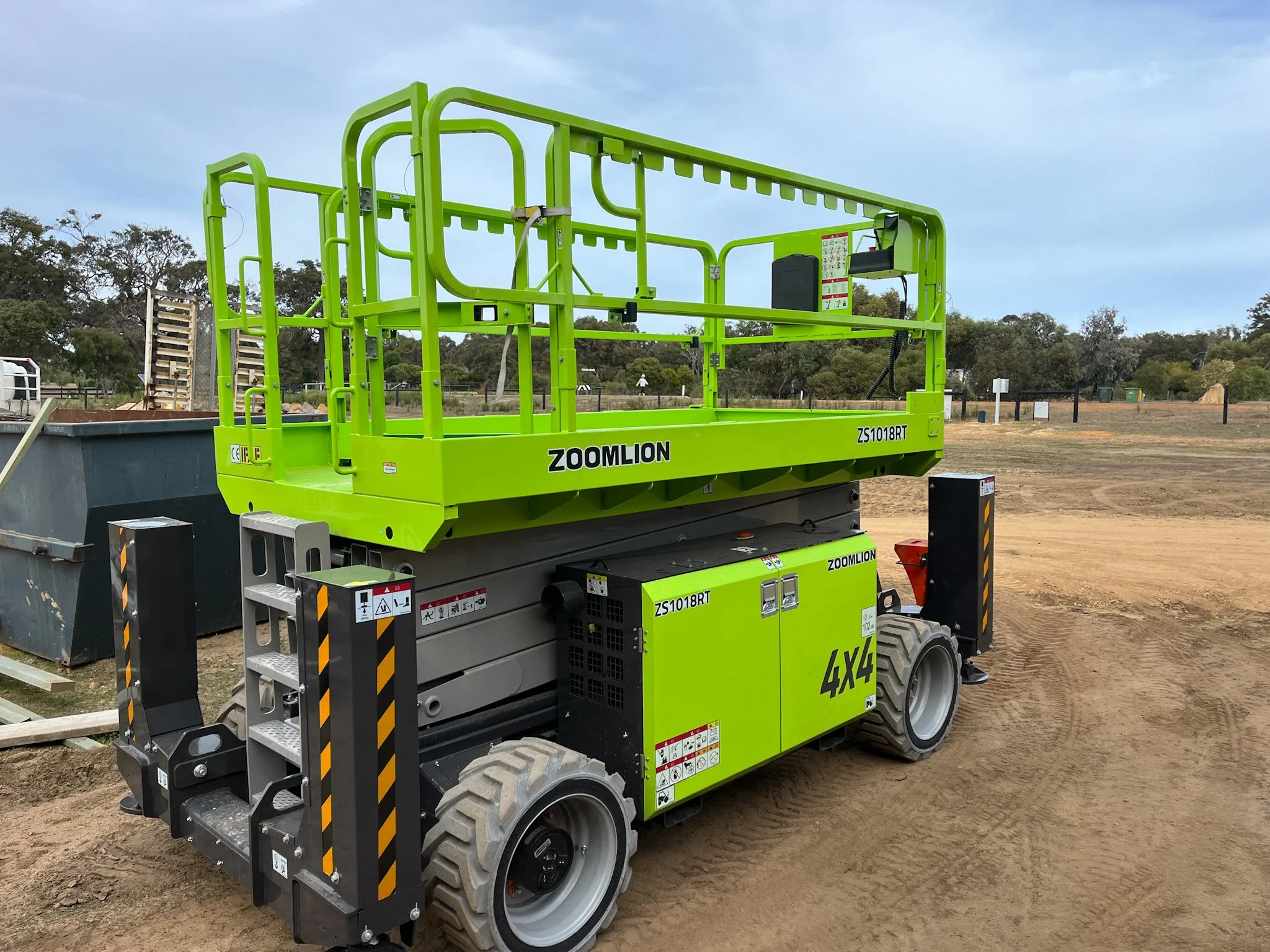 Hire Equipment Machine Western Australia South West WA - A green and gray articulated boom lift with the brand name Zoomlion on the side, parked on a dirt surface outdoors with trees in the background.