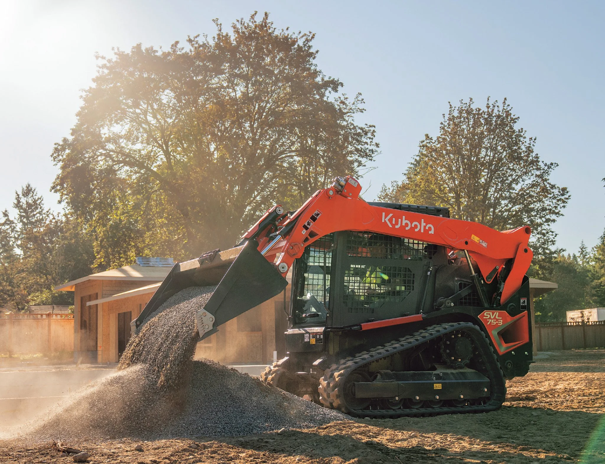 Hire Equipment Machine Western Australia South West WA - A Kubota mini excavator with a tracked undercarriage is pouring dirt onto a pile at a construction site during daytime, with trees and houses in the background.