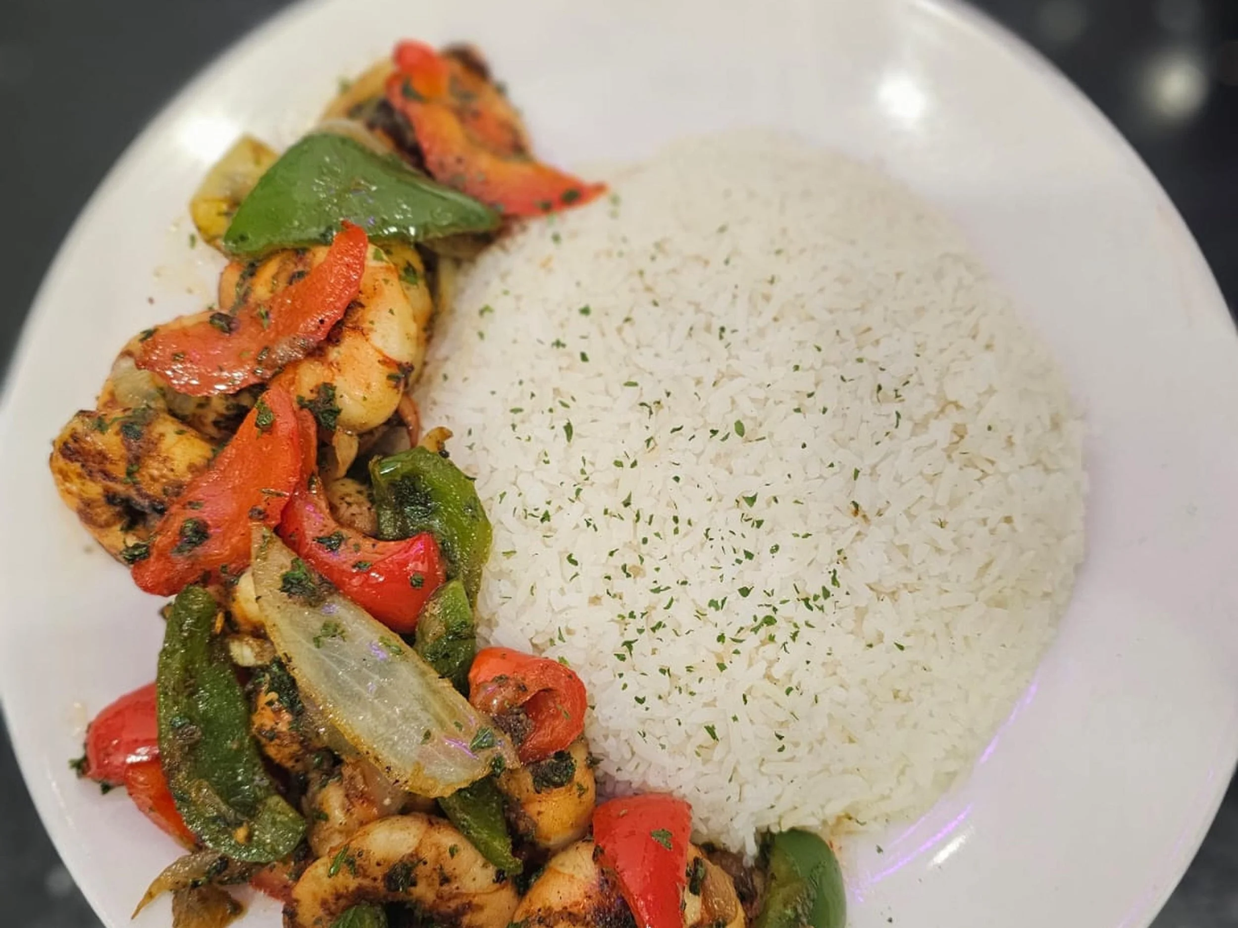 Grilled chicken breast topped with sautéed red and green bell peppers and herbs, served on a white plate with seasoned rice.