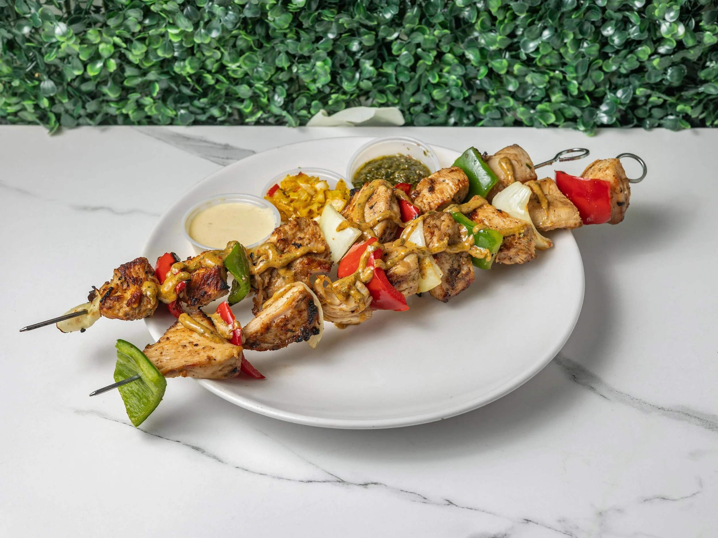 Skewers with grilled chicken and vegetables served with various sauces on a white plate.