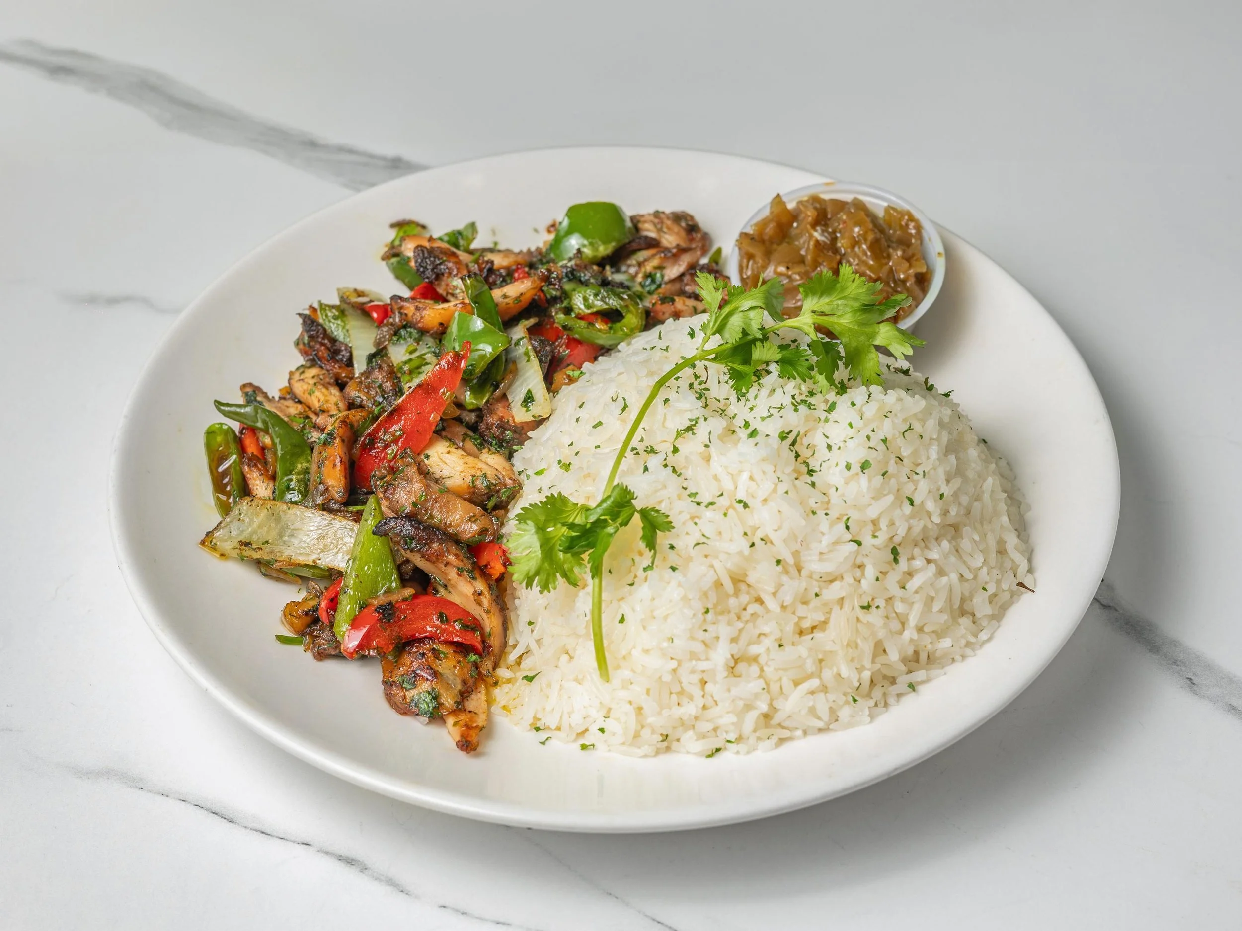 A white plate with cooked white rice garnished with cilantro, served alongside a stir-fried vegetable and chicken dish with red and green peppers, and a small side container of brownish pickled vegetables or chutney.